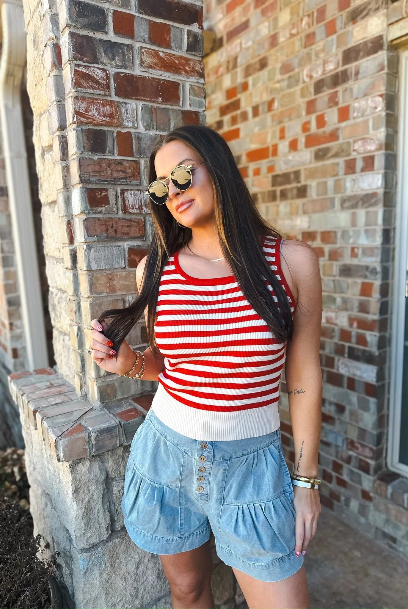 Woman wearing a red and white striped ribbed tank top and light blue ruffled button-front shorts, accessorized with