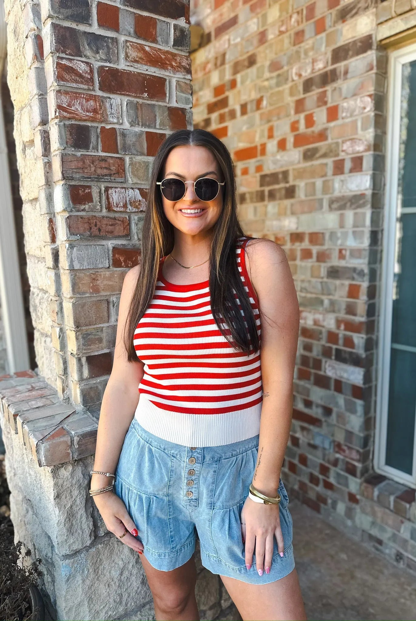 Woman wearing a cream and red stripe game day tank top and light wash denim shorts with buttons.