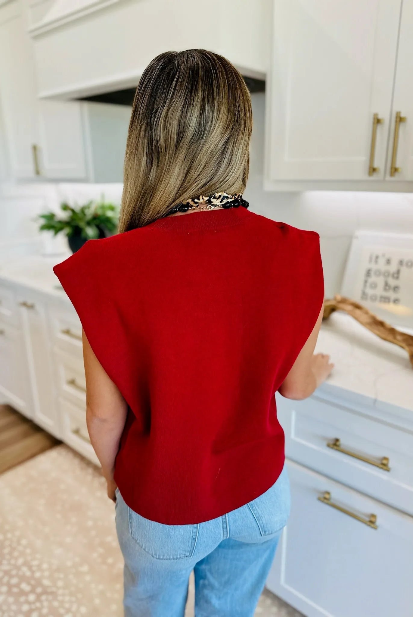 Back view of a woman wearing a crimson round neck cap sleeve sweater over light wash jeans, accessorized with a chunky