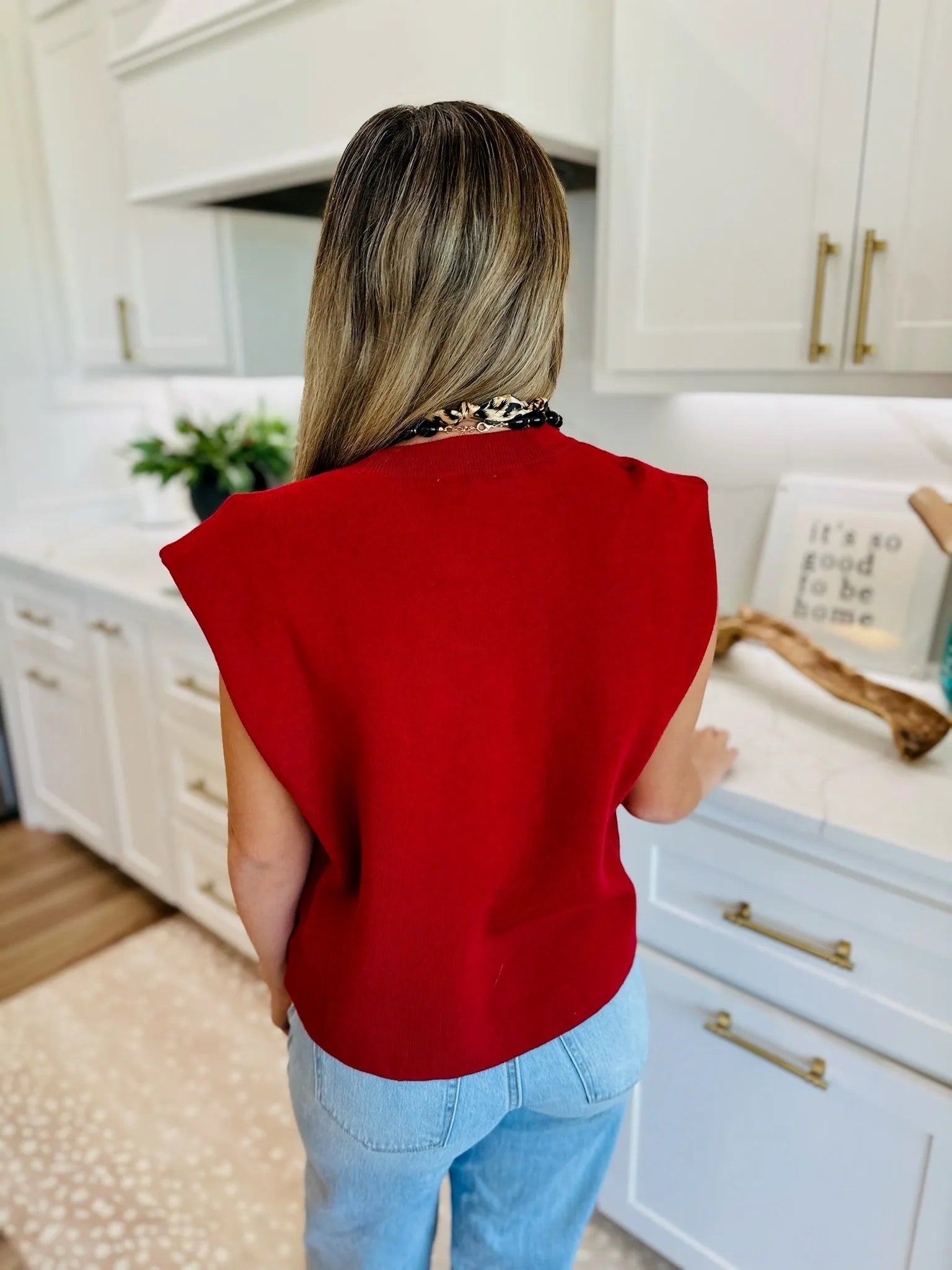 Back view of a woman wearing a crimson round neck cap sleeve sweater over light wash jeans, accessorized with a chunky