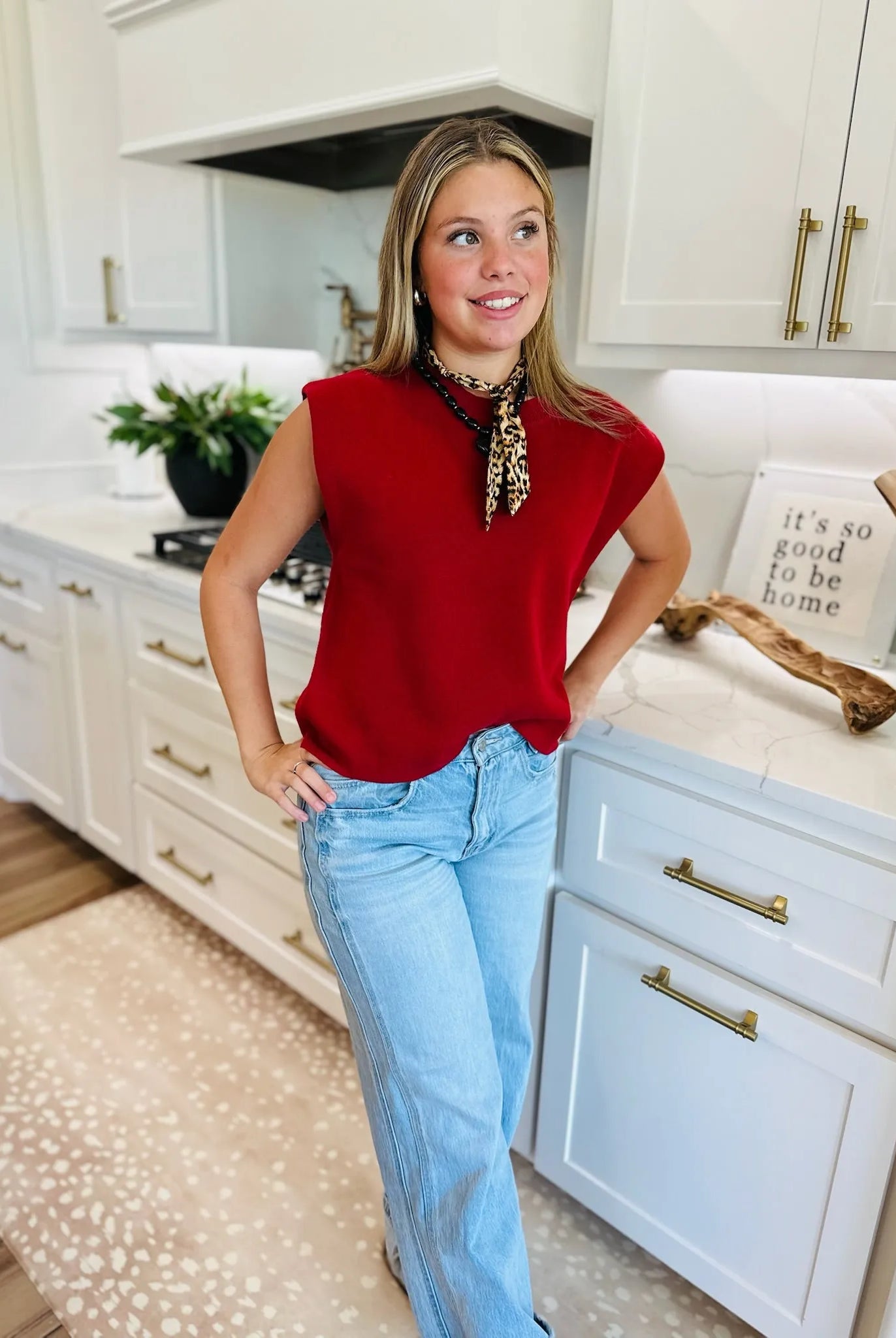 Woman wearing a crimson round neck, cap sleeve sweater and light wash wide-leg jeans, accessorized with a leopard print