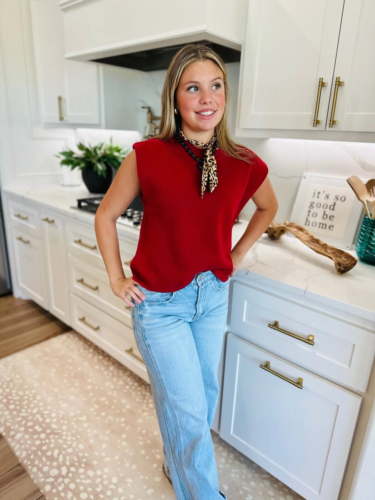 Woman wearing a crimson round neck, cap sleeve sweater and light wash wide-leg jeans, accessorized with a leopard print