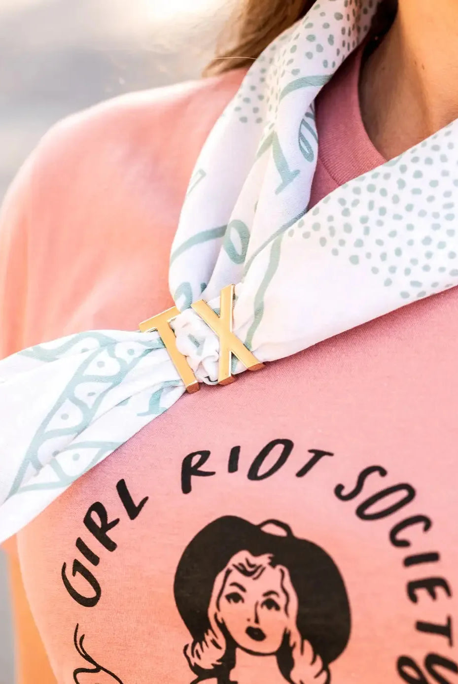 Gold TX bandana slide on a white and blue patterned bandana tied around a pink t-shirt.