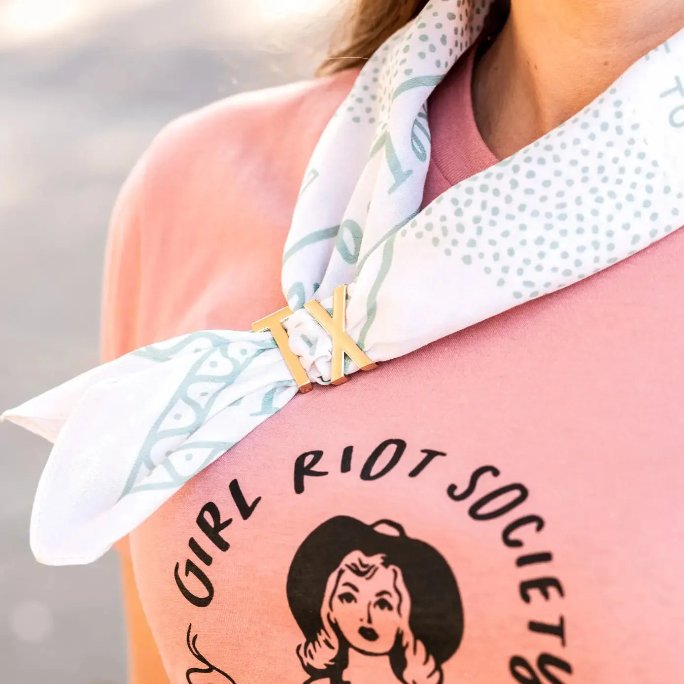 Gold TX bandana slide on a white and blue patterned bandana tied around a pink t-shirt.