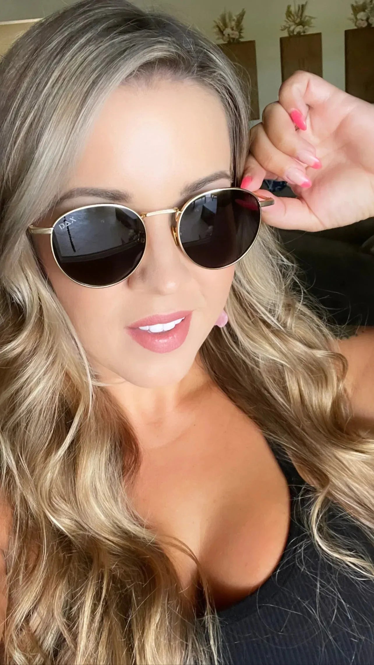 Close-up of a woman wearing DAX Eyewear Luna gold metal sunglasses with round, dark lenses. Her blonde hair is wavy.