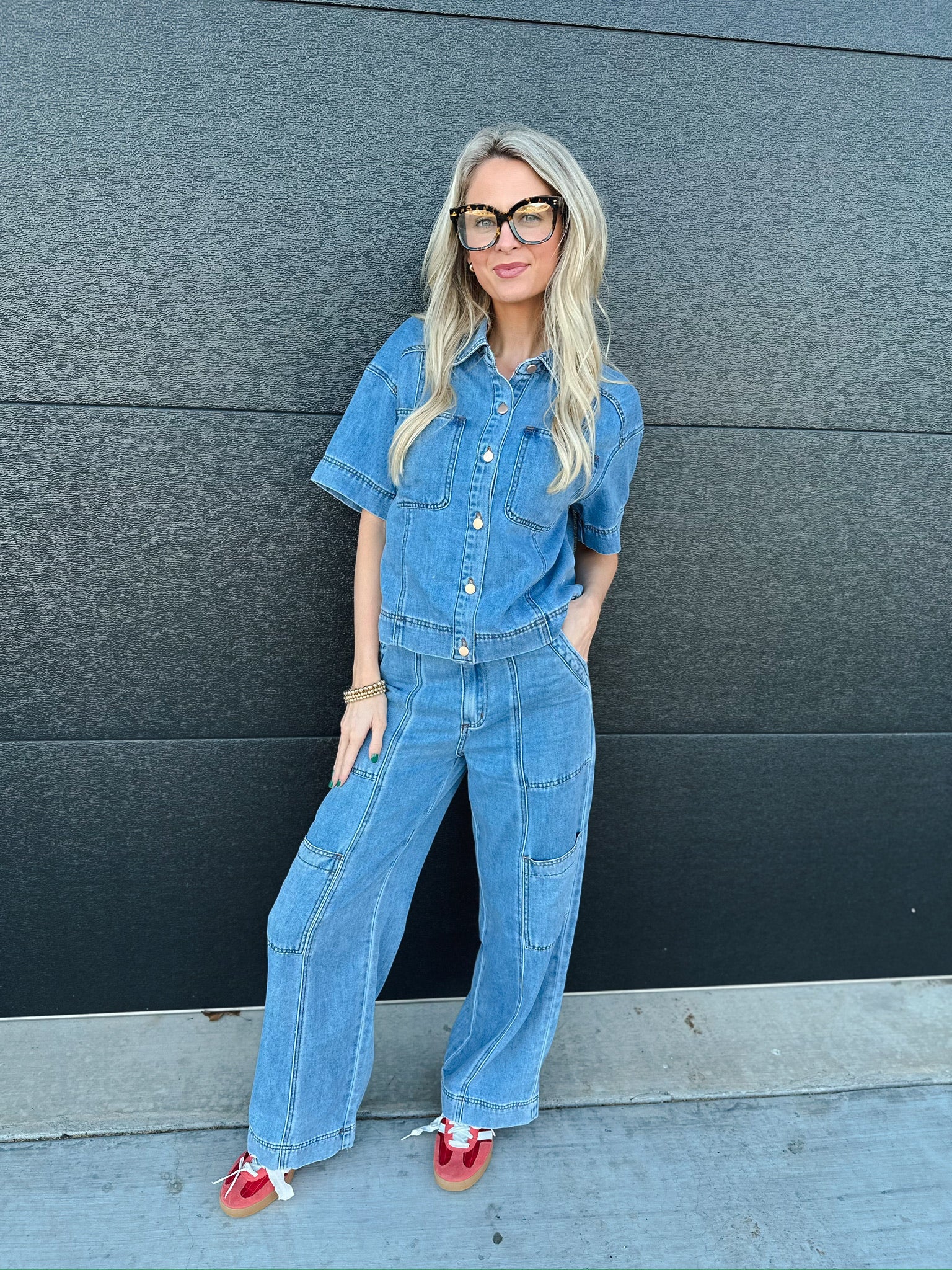 Woman wearing a light wash denim short-sleeve button-down shirt and matching wide-leg cargo pants. She has blonde hair and