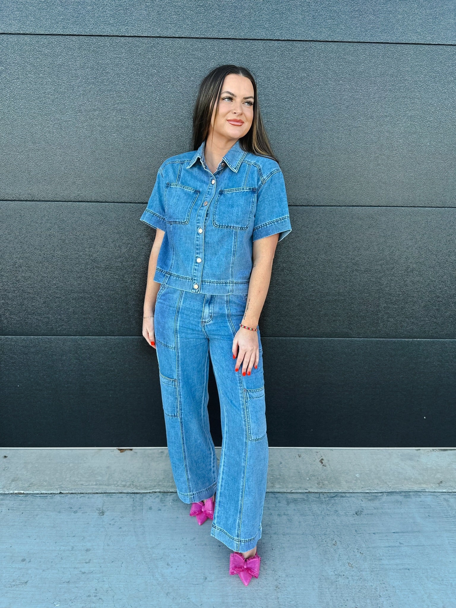 Woman wearing a light wash denim button-down shirt with short sleeves and cargo pants. She has on bright pink bow heels.