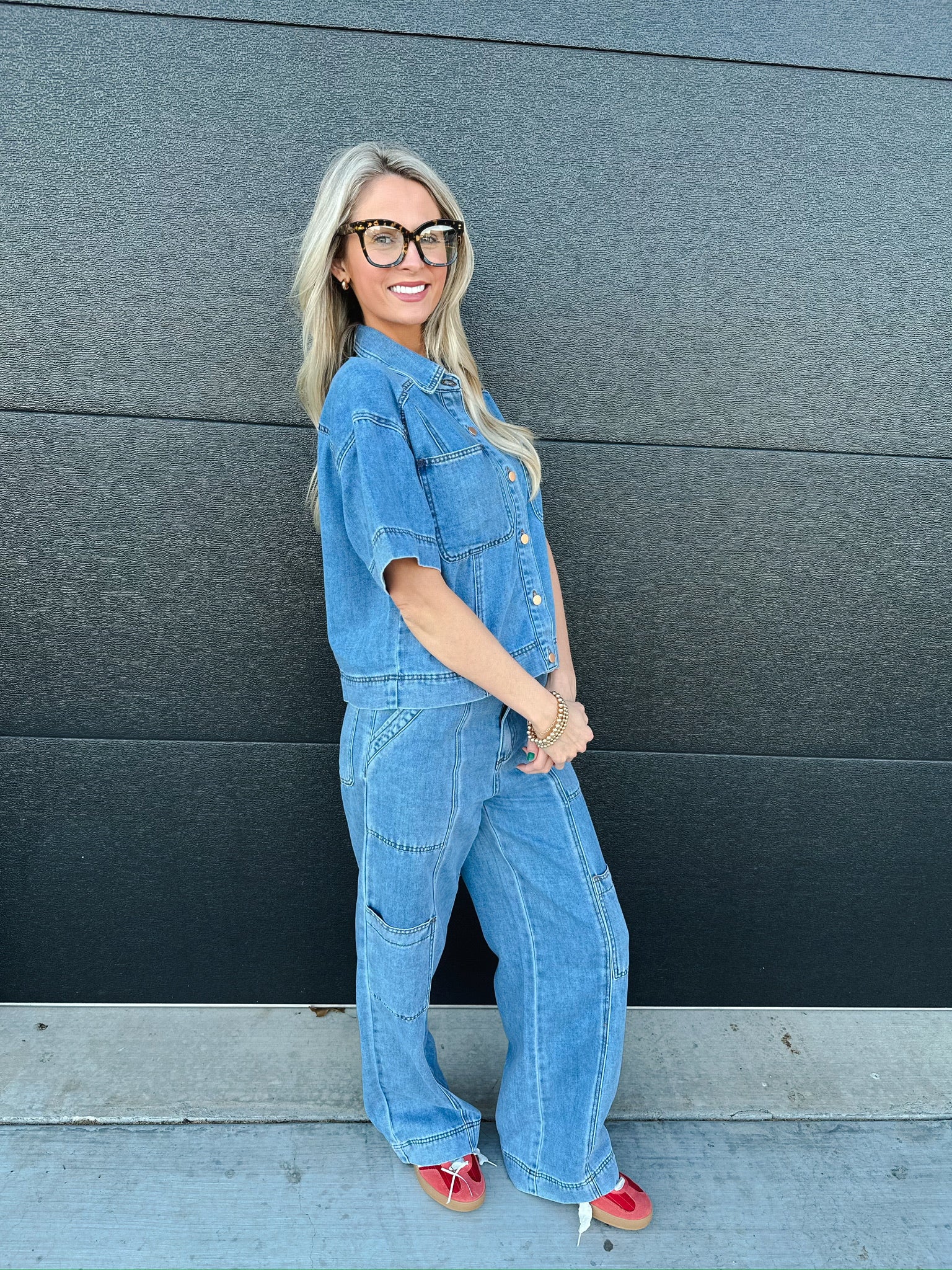 Woman wearing a light wash denim button-down shirt with short sleeves and relaxed fit cargo pants. She has blonde hair and