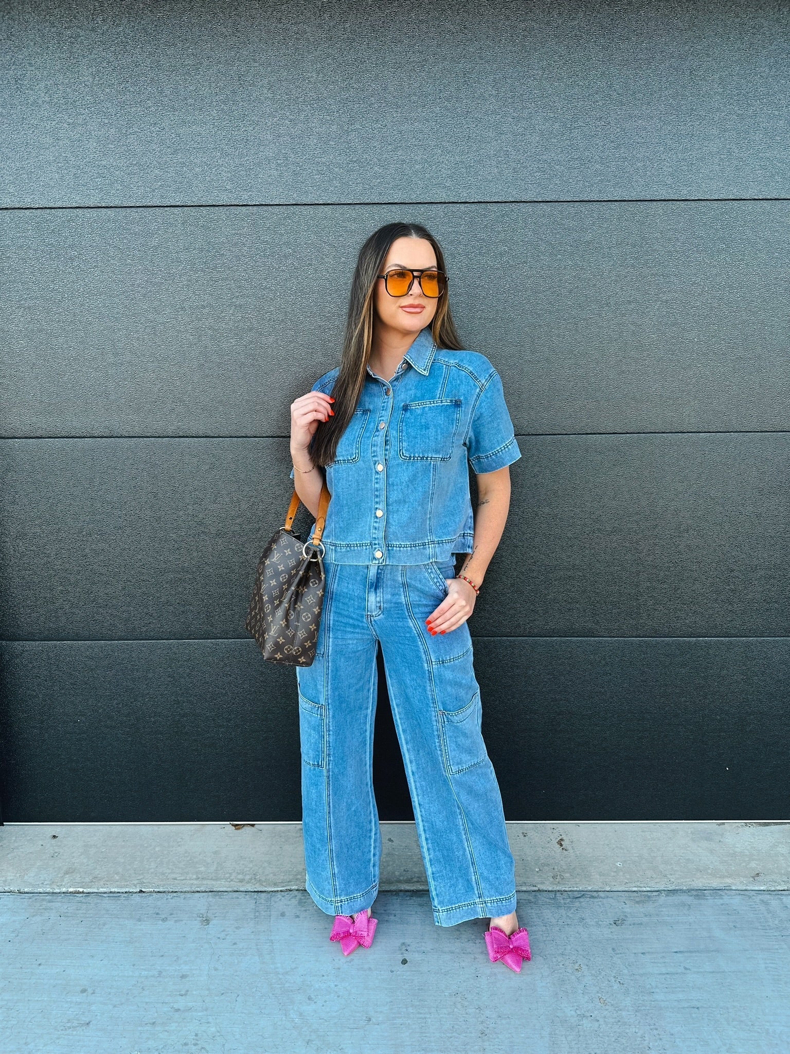 Woman wearing a light wash denim button-down shirt and matching cargo pants. She accessorizes with orange sunglasses and