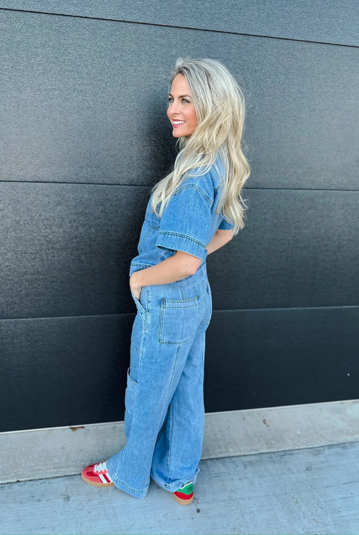 Woman in light wash denim button-down shirt and matching wide-leg cargo pants, with red and green sneakers.
