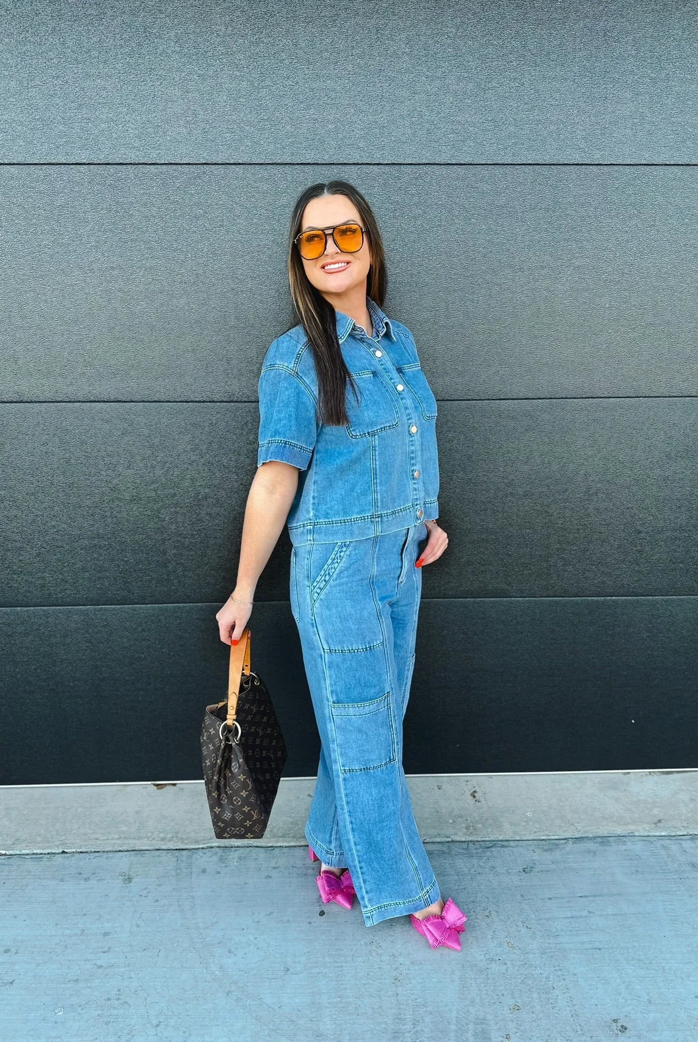 Woman in a blue denim button-down shirt and cargo pants, holding a designer handbag, wearing orange sunglasses and bright