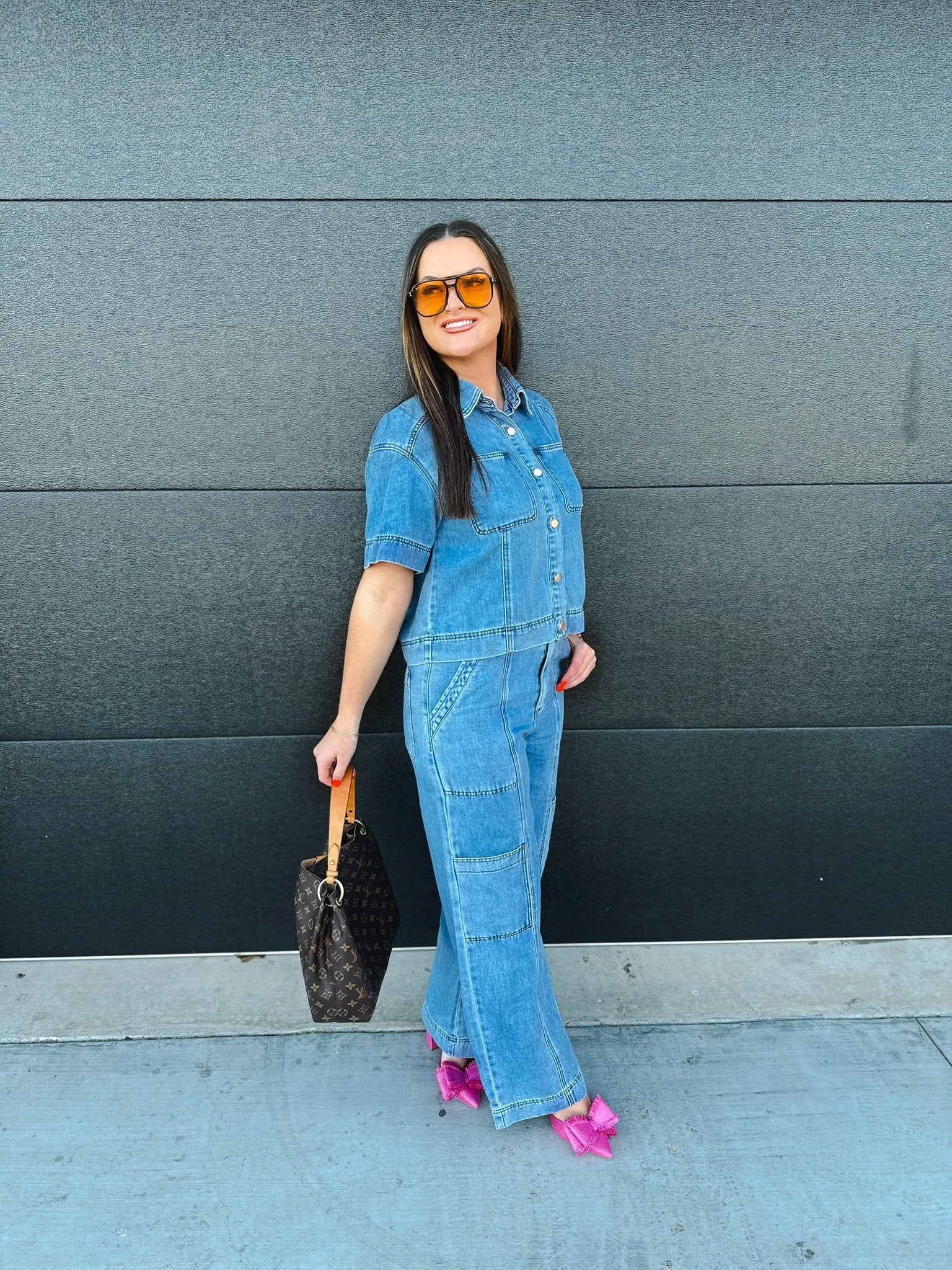 Woman in a blue denim button-down shirt and cargo pants, holding a designer handbag, wearing orange sunglasses and bright