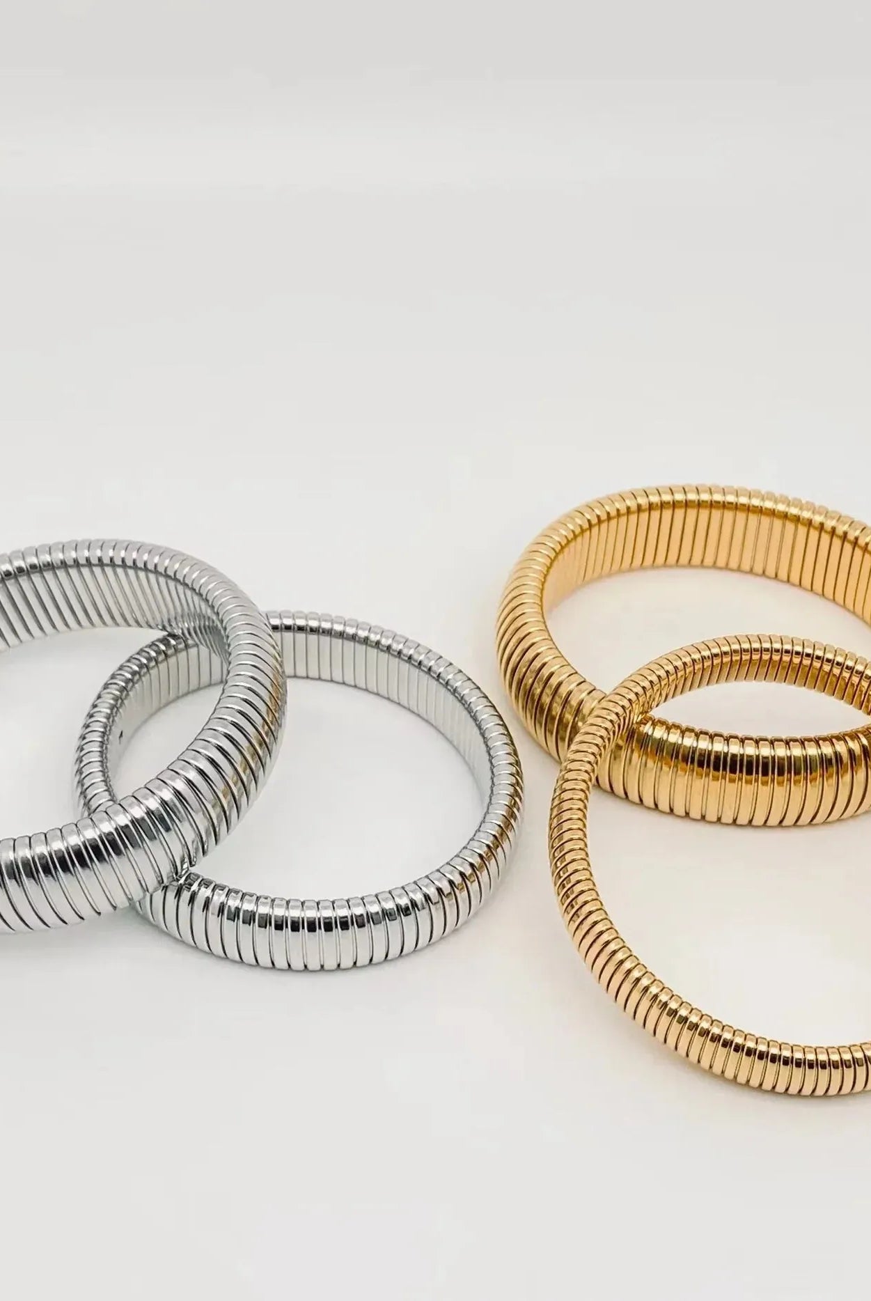 Two gold-plated and two stainless steel elastic bangles with ribbed texture, displayed on a white background.