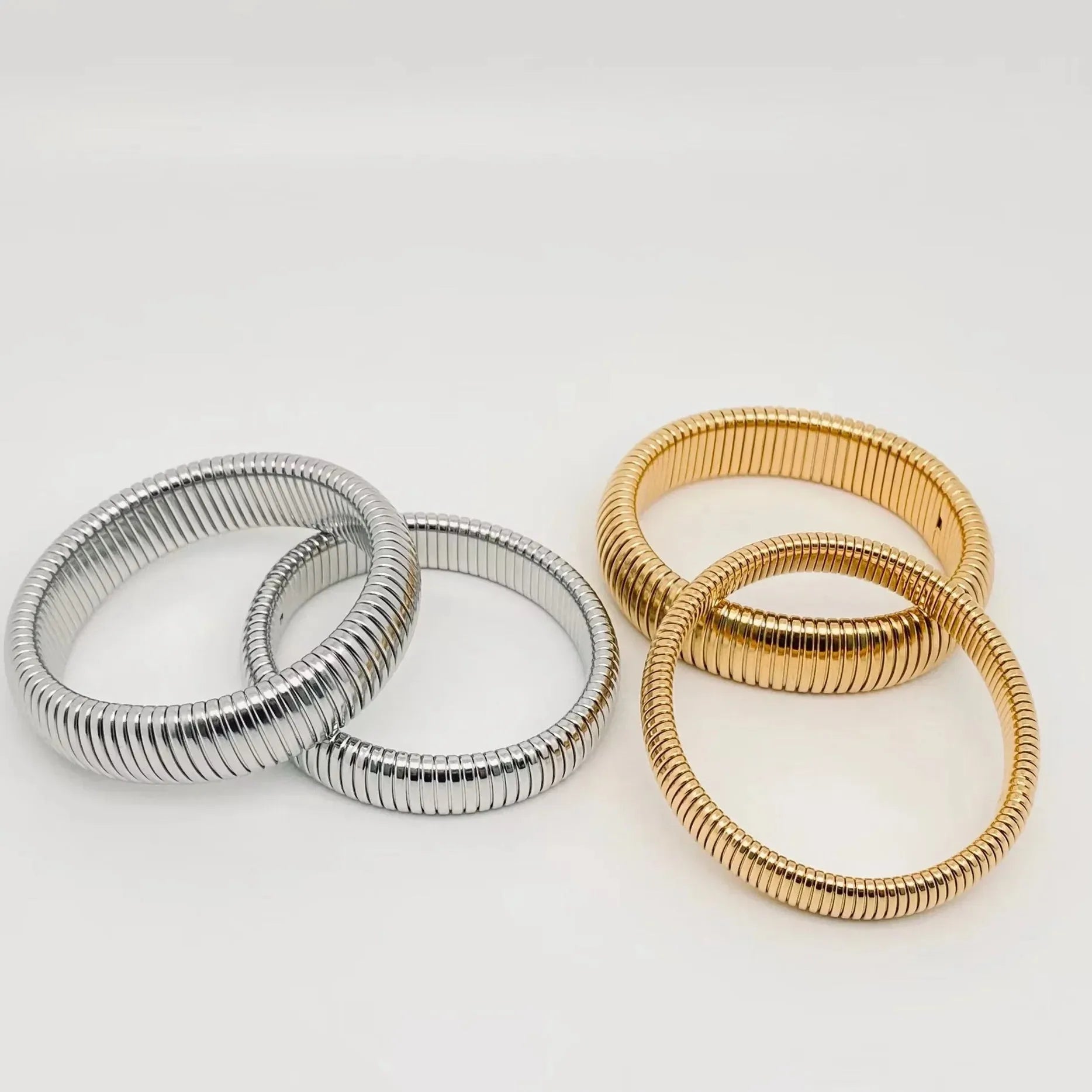 Two gold-plated and two stainless steel elastic bangles with ribbed texture, displayed on a white background.