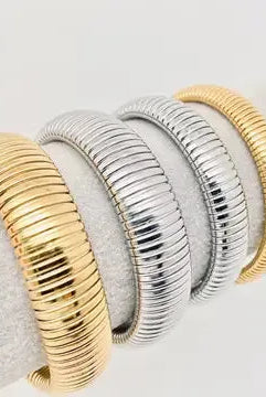 Gold plated and silver stainless steel elastic bangles with ribbed texture displayed on white fabric.