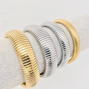 Gold plated and silver stainless steel elastic bangles with ribbed texture displayed on white fabric.