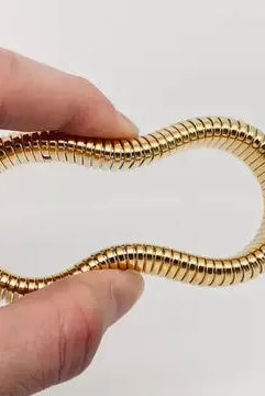 Close-up of a flexible, shiny gold plated stainless steel bangle bracelet with a ribbed texture, held in a hand.