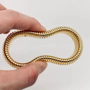 Close-up of a flexible, shiny gold plated stainless steel bangle bracelet with a ribbed texture, held in a hand.