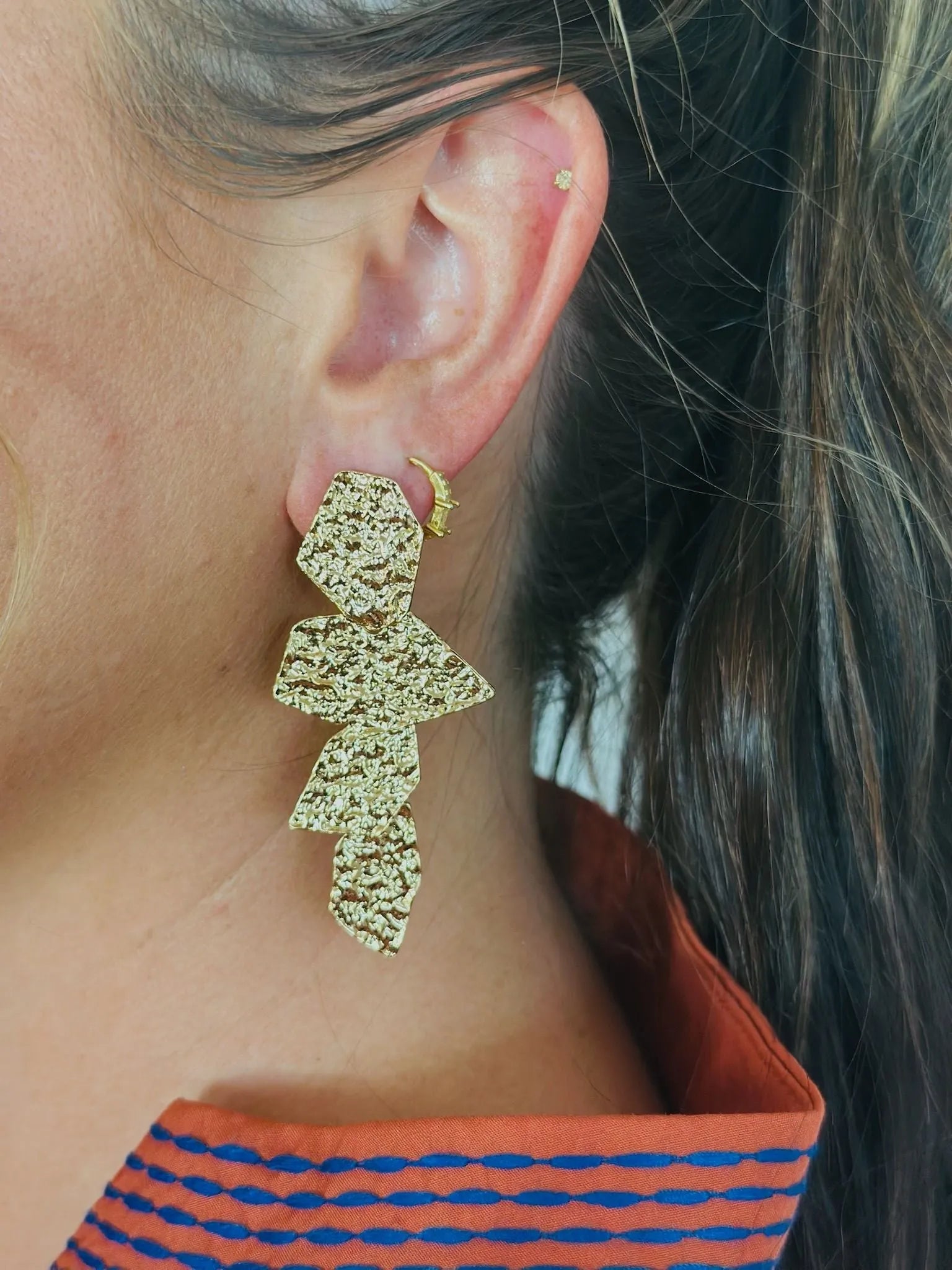 Electra statement earrings in hammered gold finish. Abstract, multi-layered geometric design with textured surface. Worn on