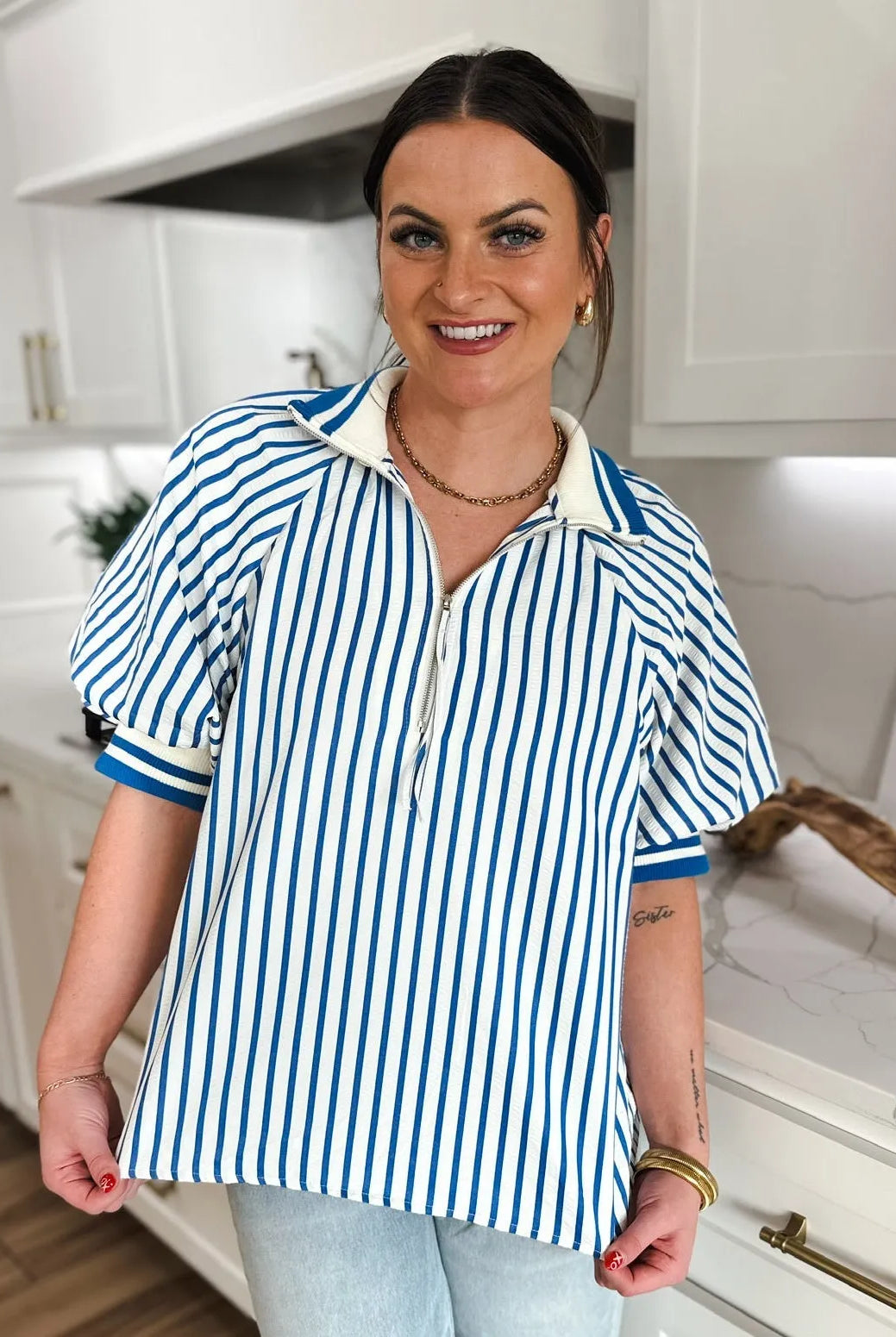 Woman wearing a blue and white striped zip V-neck top with short puffy sleeves and a white collar.