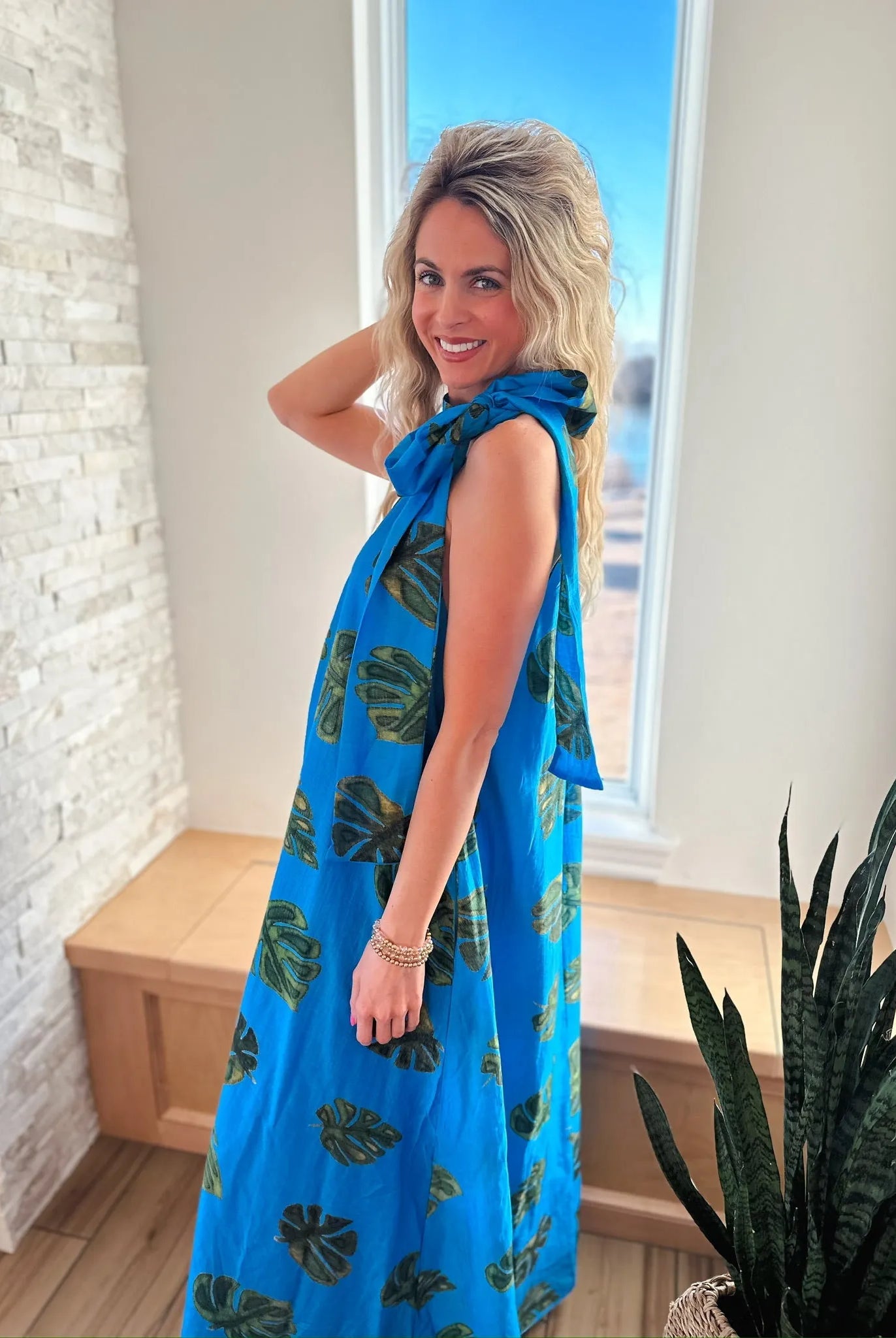 Entro blue maxi dress with green palm leaf print and tie neck. Sleeveless, flowy, full-length dress on a woman.