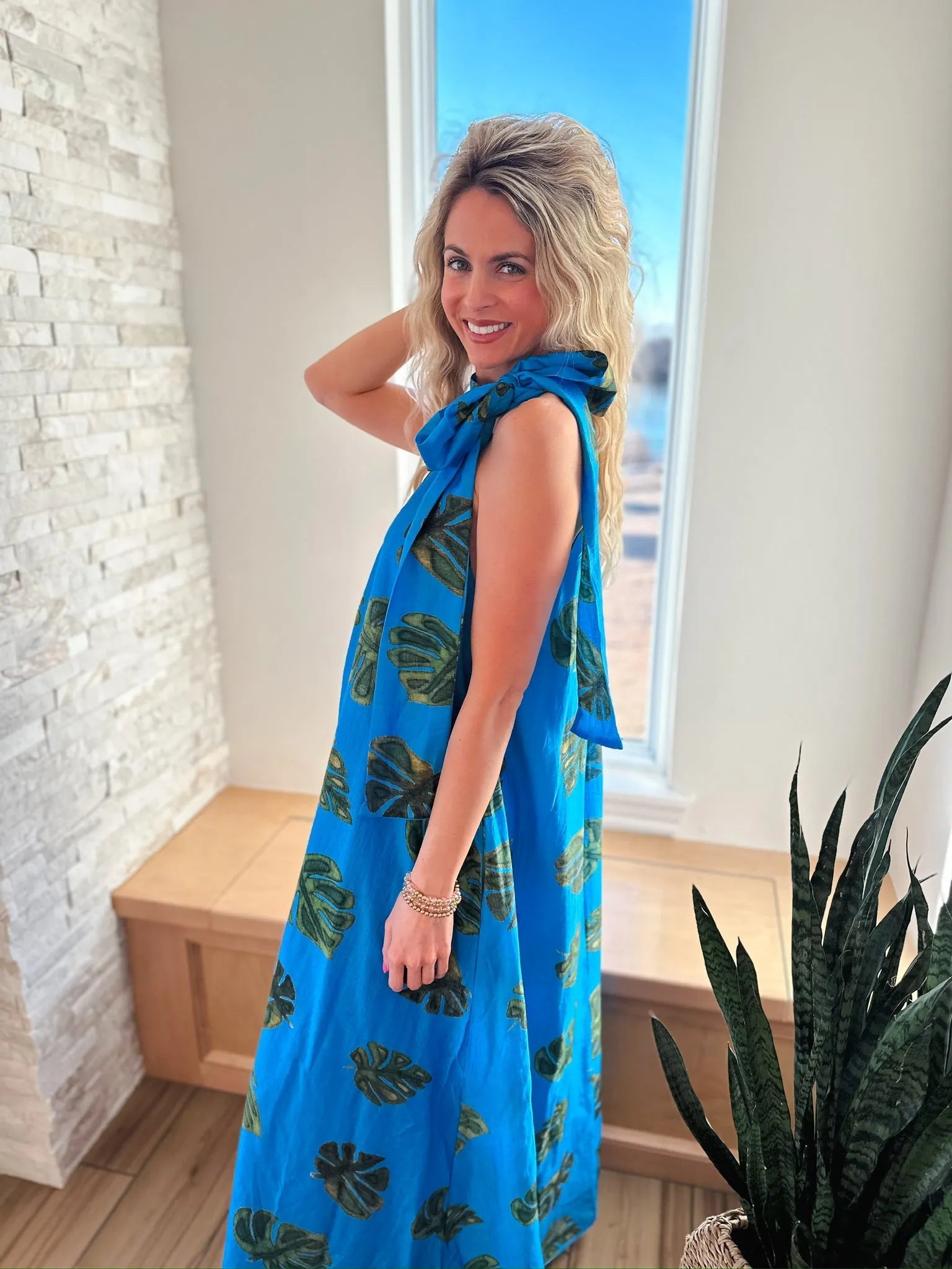 Entro blue maxi dress with green palm leaf print and tie neck. Sleeveless, flowy, full-length dress on a woman.