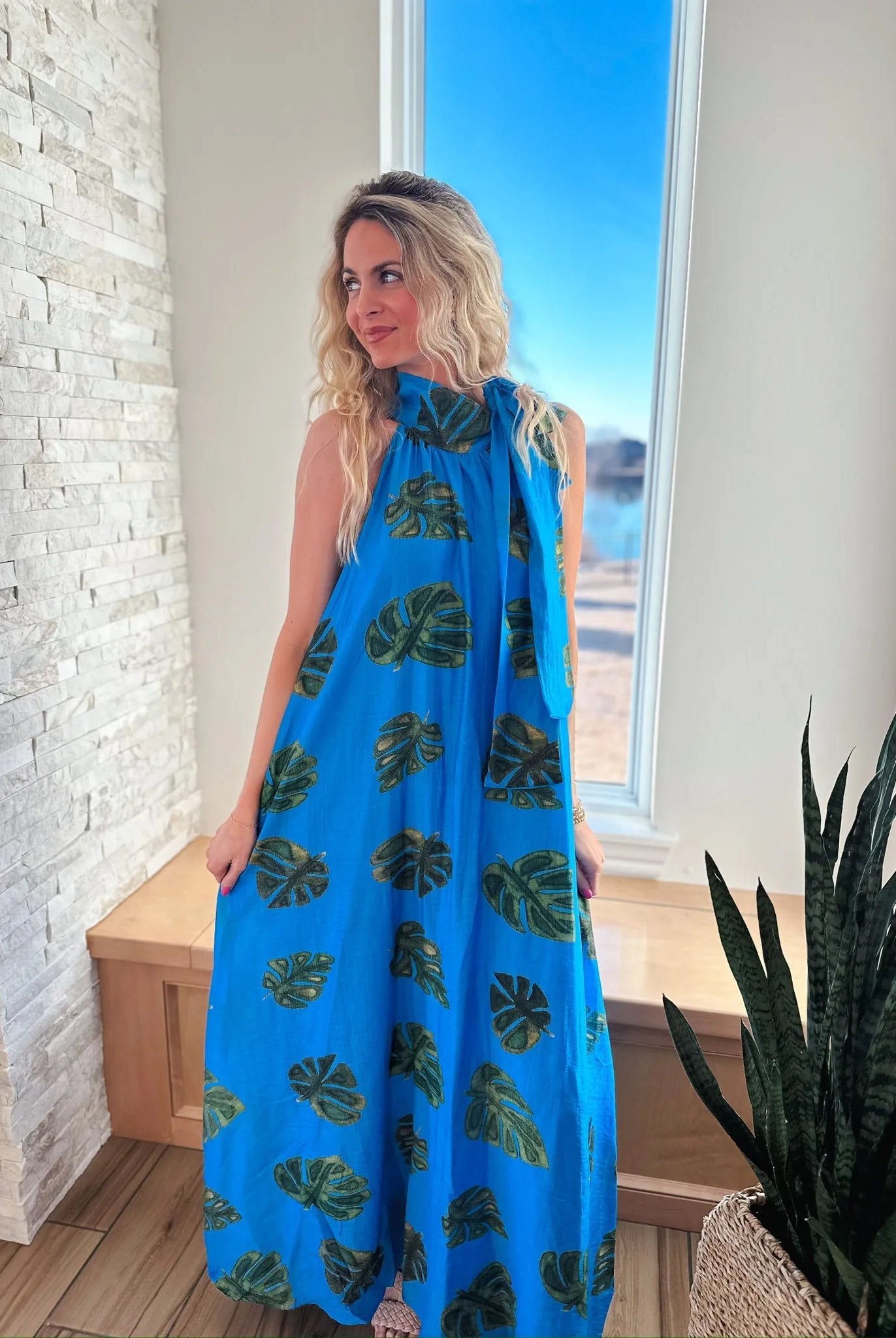 Entro blue maxi dress with a tie neck and a tropical palm leaf print. Sleeveless, floor-length design.