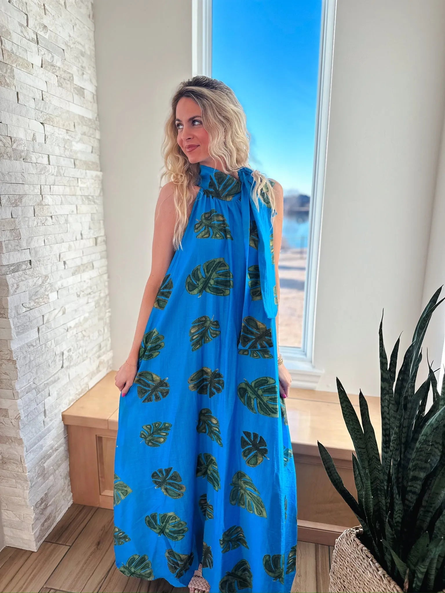 Entro blue maxi dress with a tie neck and a tropical palm leaf print. Sleeveless, floor-length design.