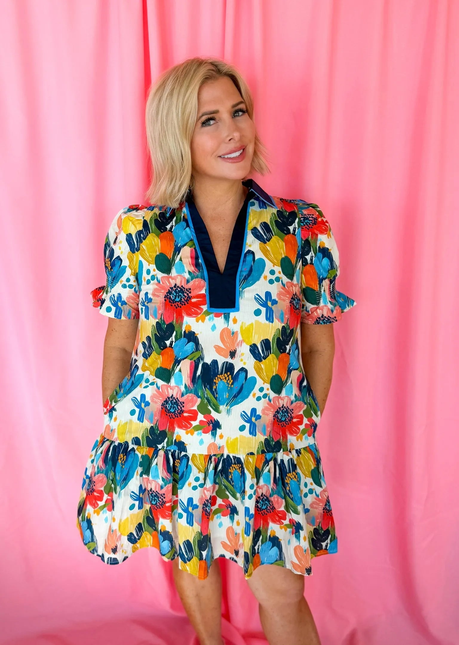 Woman wearing a blue spring flower print dress with white background, navy v-neck collar, and puff sleeves.