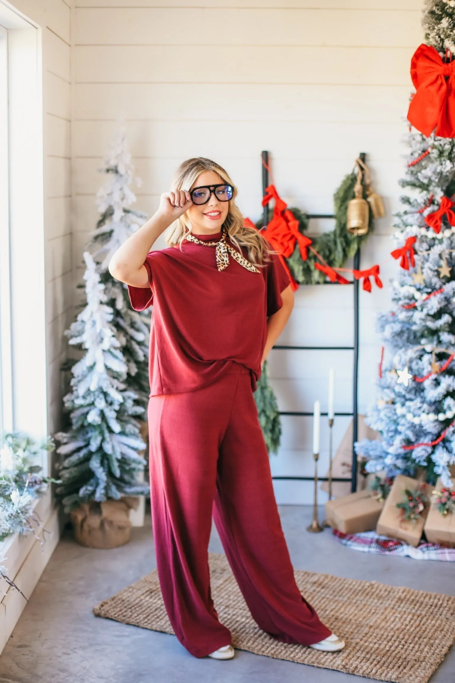 Woman in burgundy ribbed matching set with wide-leg pants and short-sleeve top, wearing glasses and leopard print scarf.