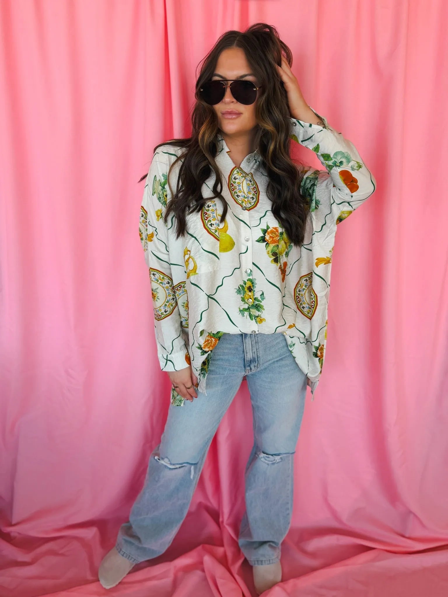 Woman wearing a white oversized button-down top with a vibrant citrus and floral print, paired with light wash ripped jeans