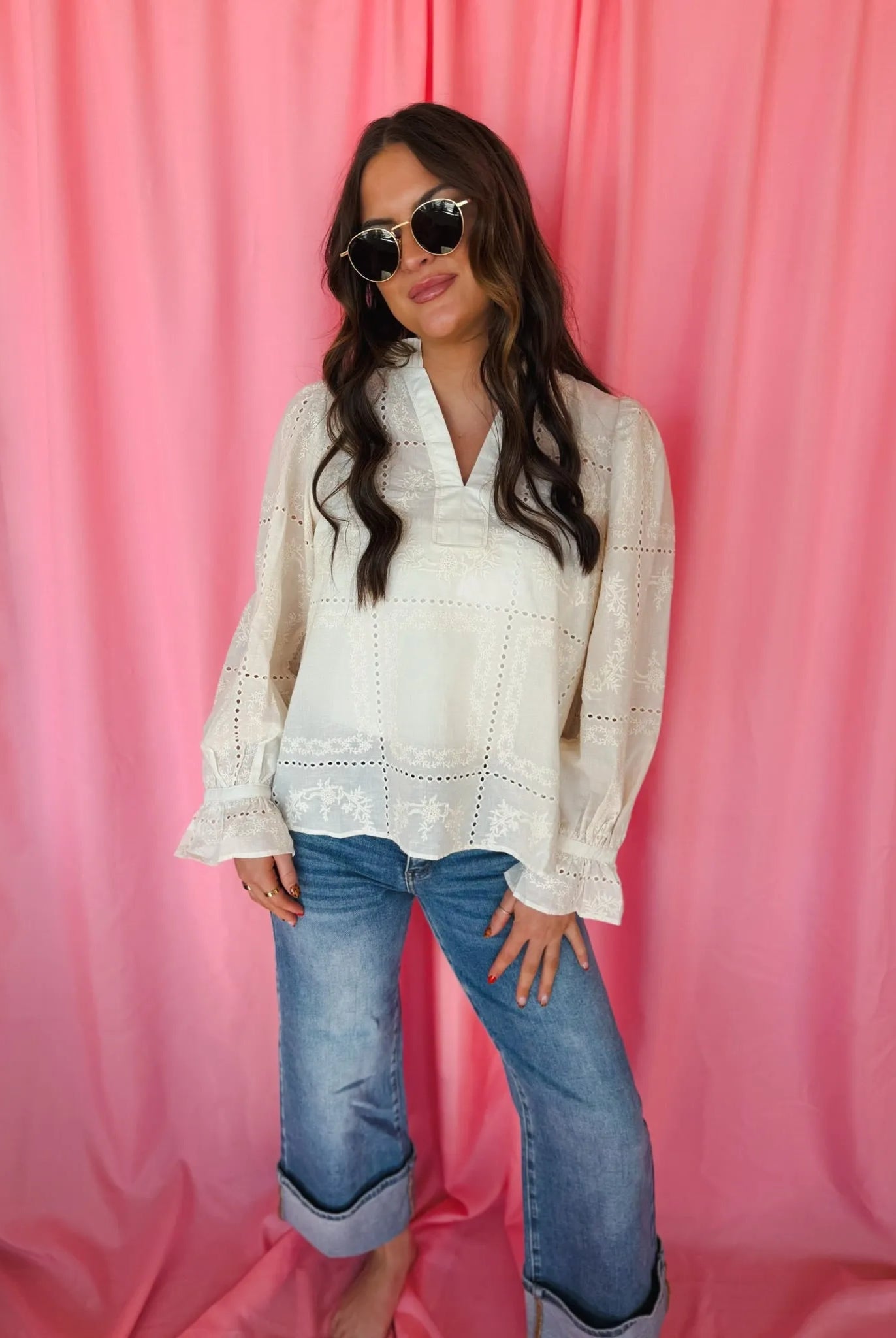 Entro cream eyelet long sleeve blouse with v-neck, eyelet embroidery details, and ruffled cuffs. Model wears blue cuffed