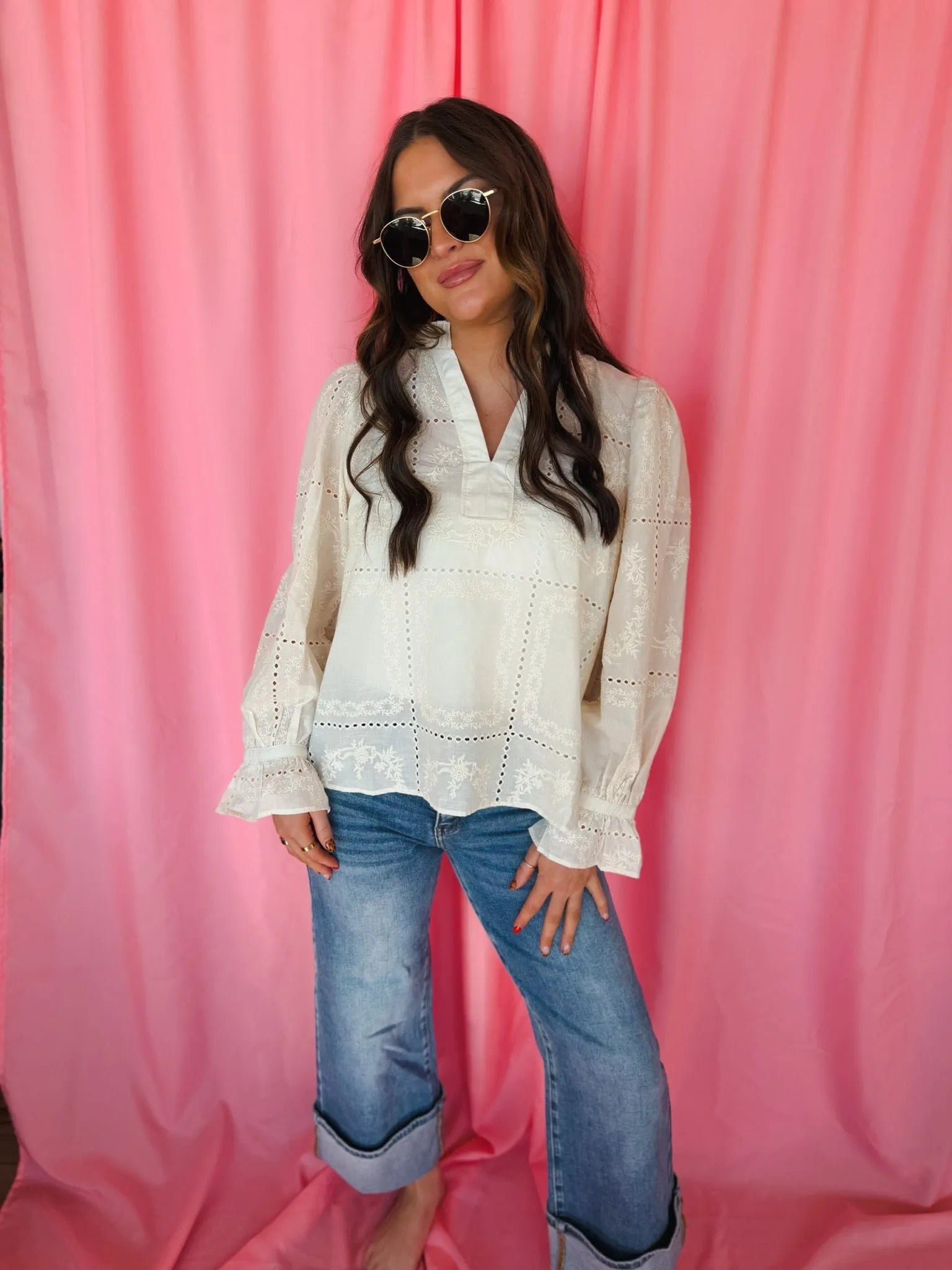 Entro cream eyelet long sleeve blouse with v-neck, eyelet embroidery details, and ruffled cuffs. Model wears blue cuffed