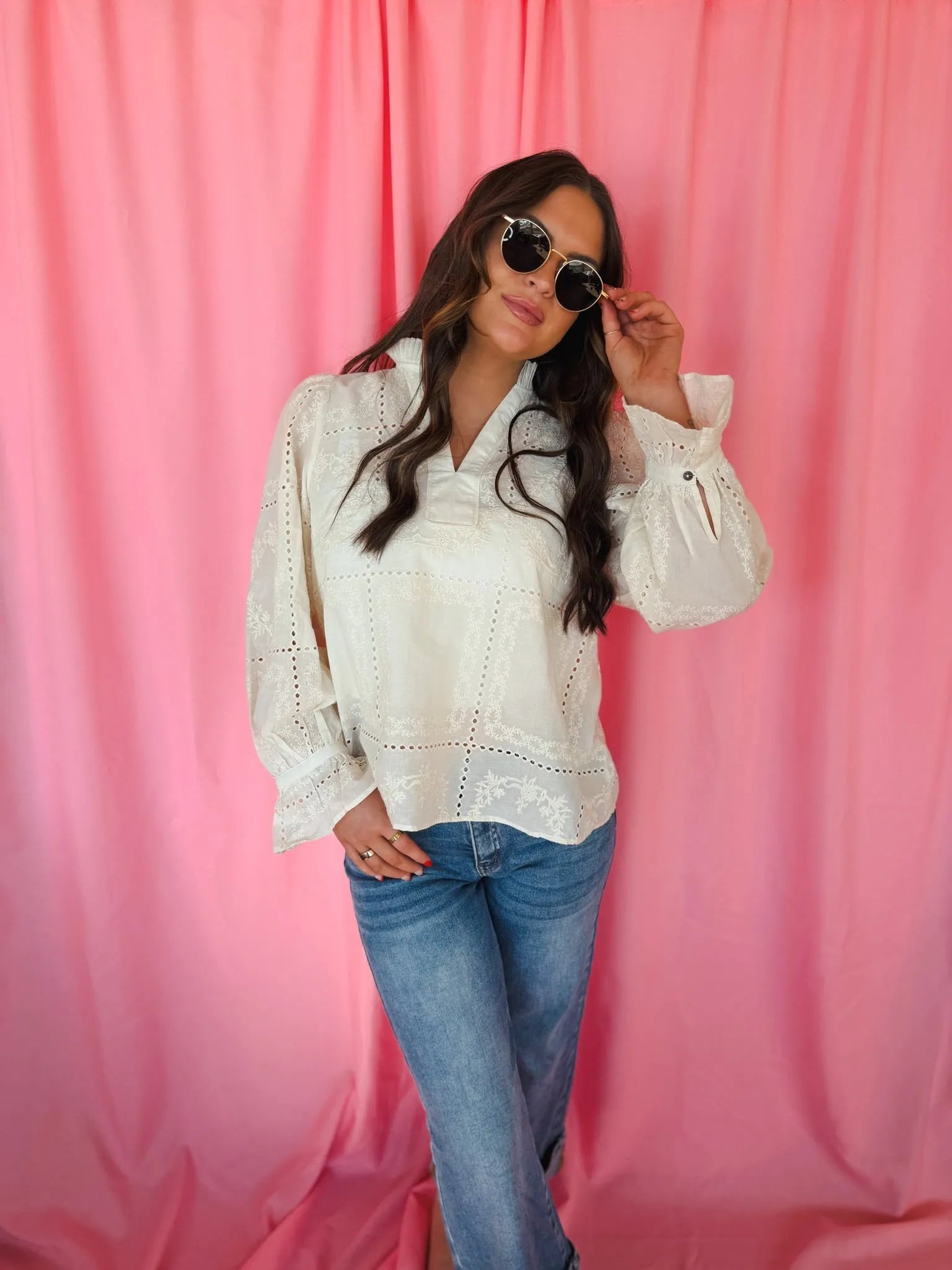 Entro cream eyelet long sleeve blouse with v-neck and ruffled cuffs, worn by a woman with sunglasses and blue jeans.