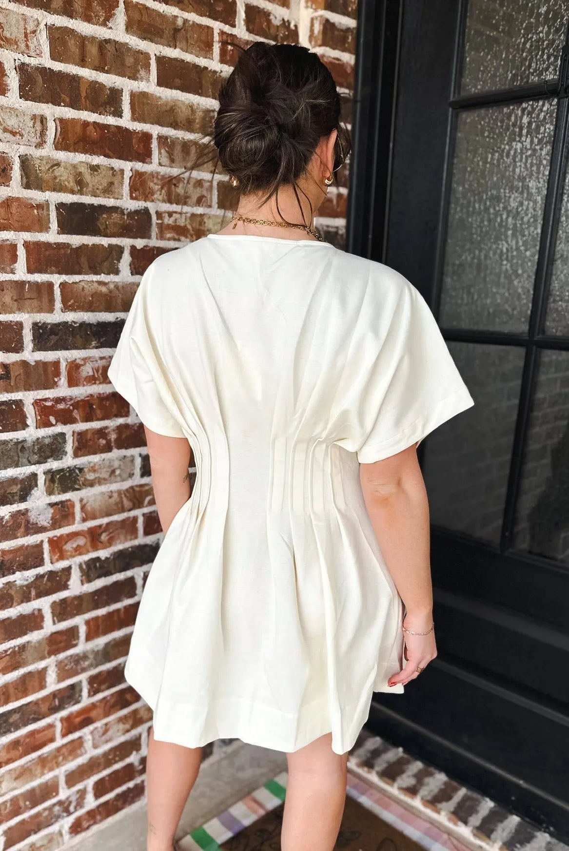 Cream dress with deep V neck, short sleeves, and pleated details on back. Pockets are implied.