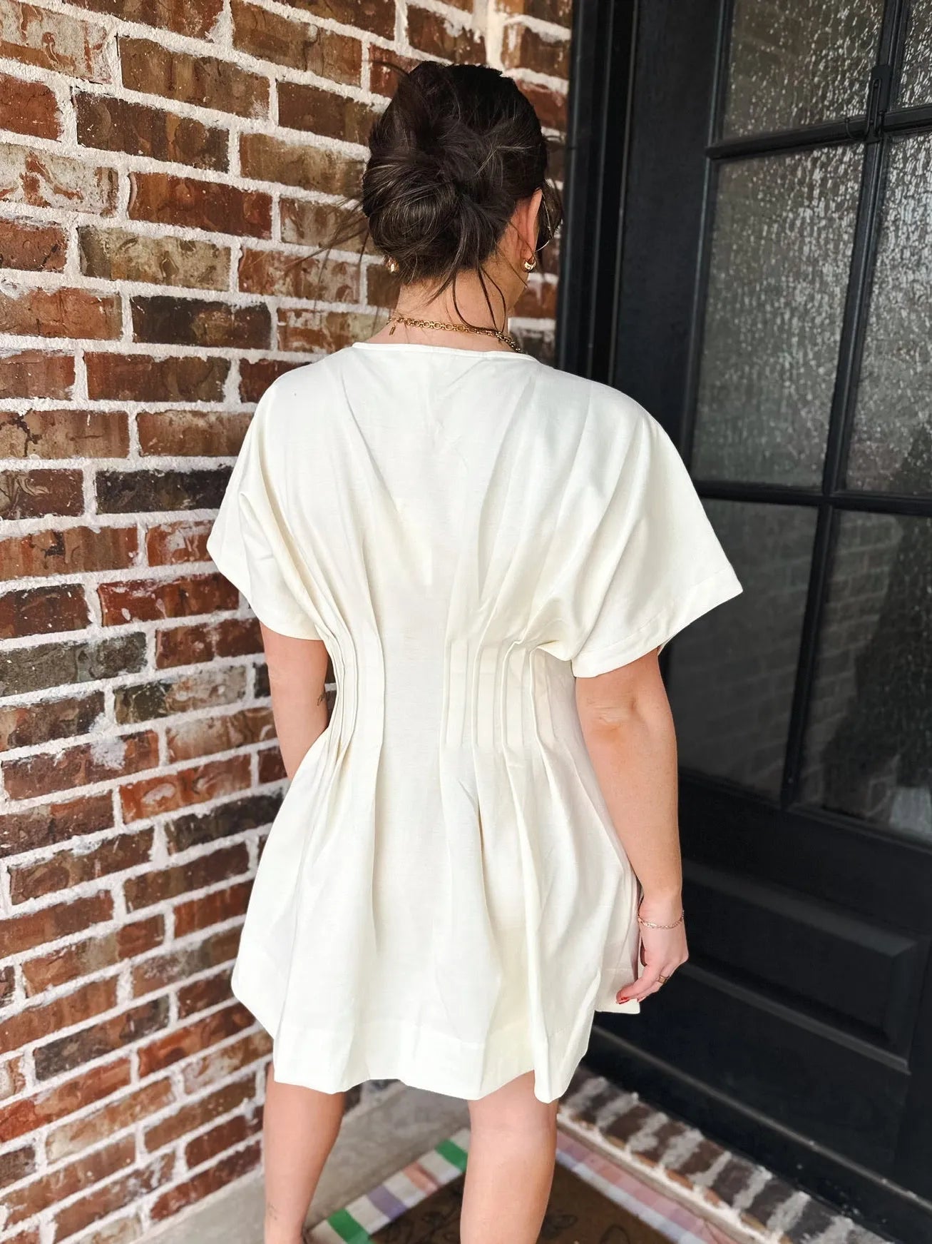 Cream dress with deep V neck, short sleeves, and pleated details on back. Pockets are implied.