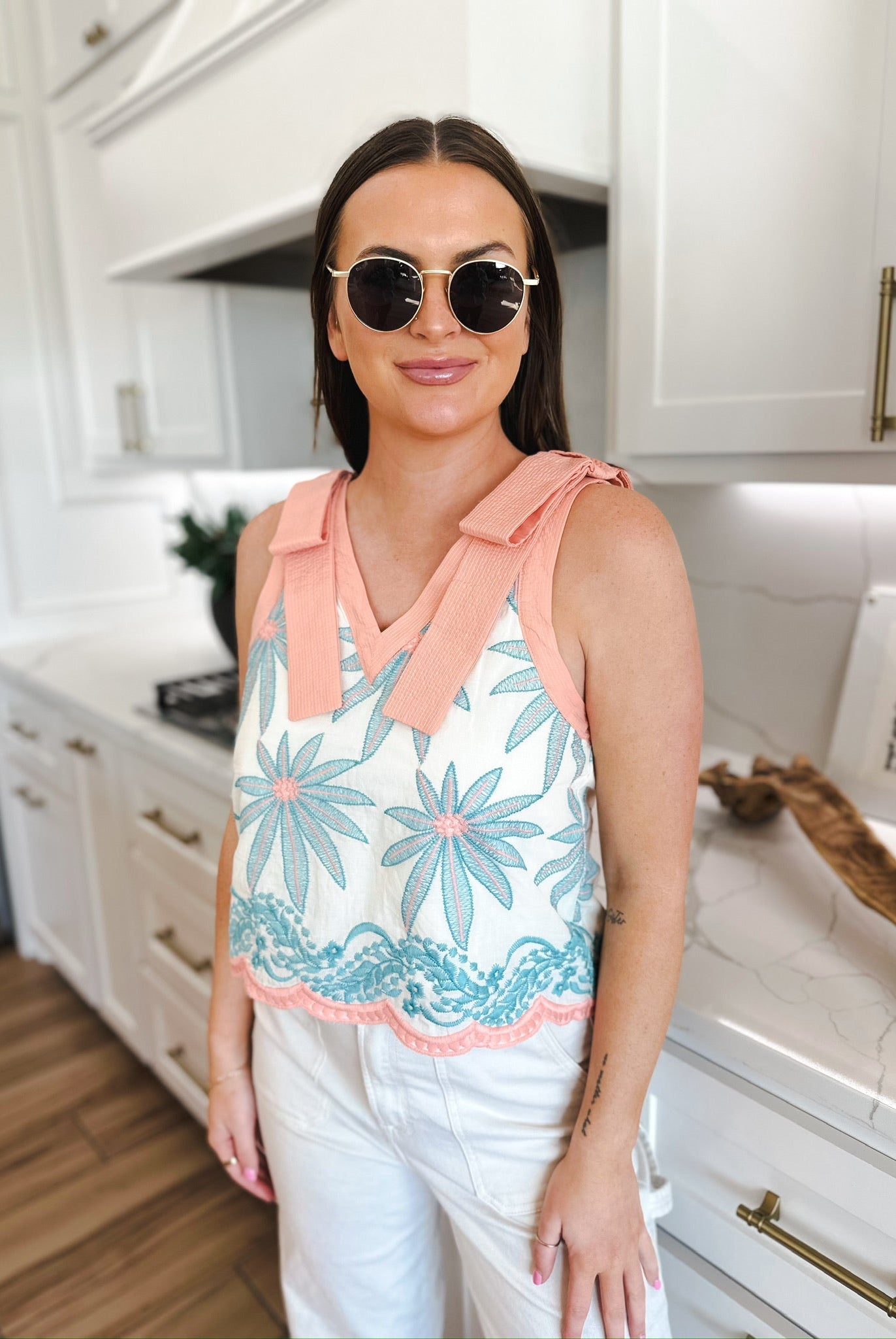 Entro white sleeveless blouse with pink trim and blue floral embroidery. Features V-neck with tie straps and scalloped hem.