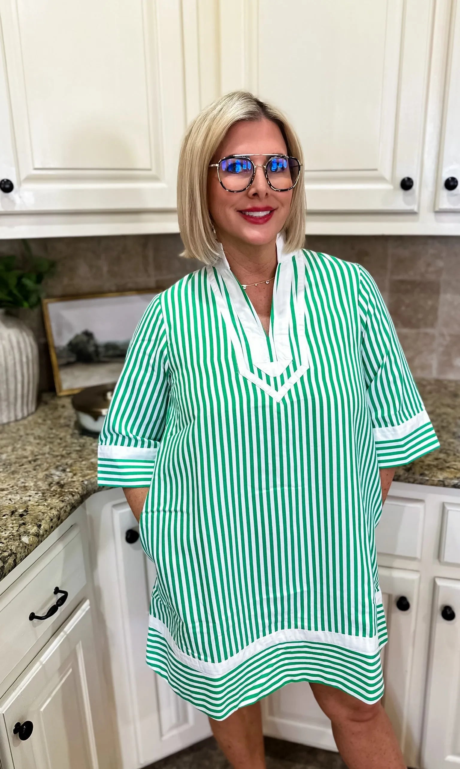 Entro green and white vertical stripe mini dress with a V-neck and cuffed sleeves. Woman wearing glasses stands in a kitchen.