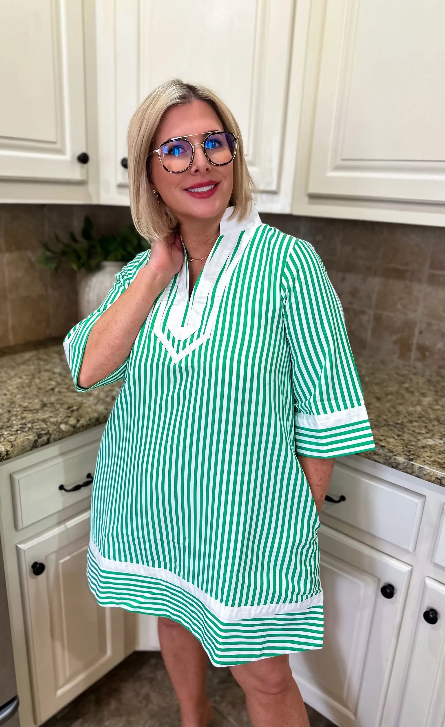 Woman wearing a green and white striped mini dress with a V-neck and white trim. The dress has short sleeves and is