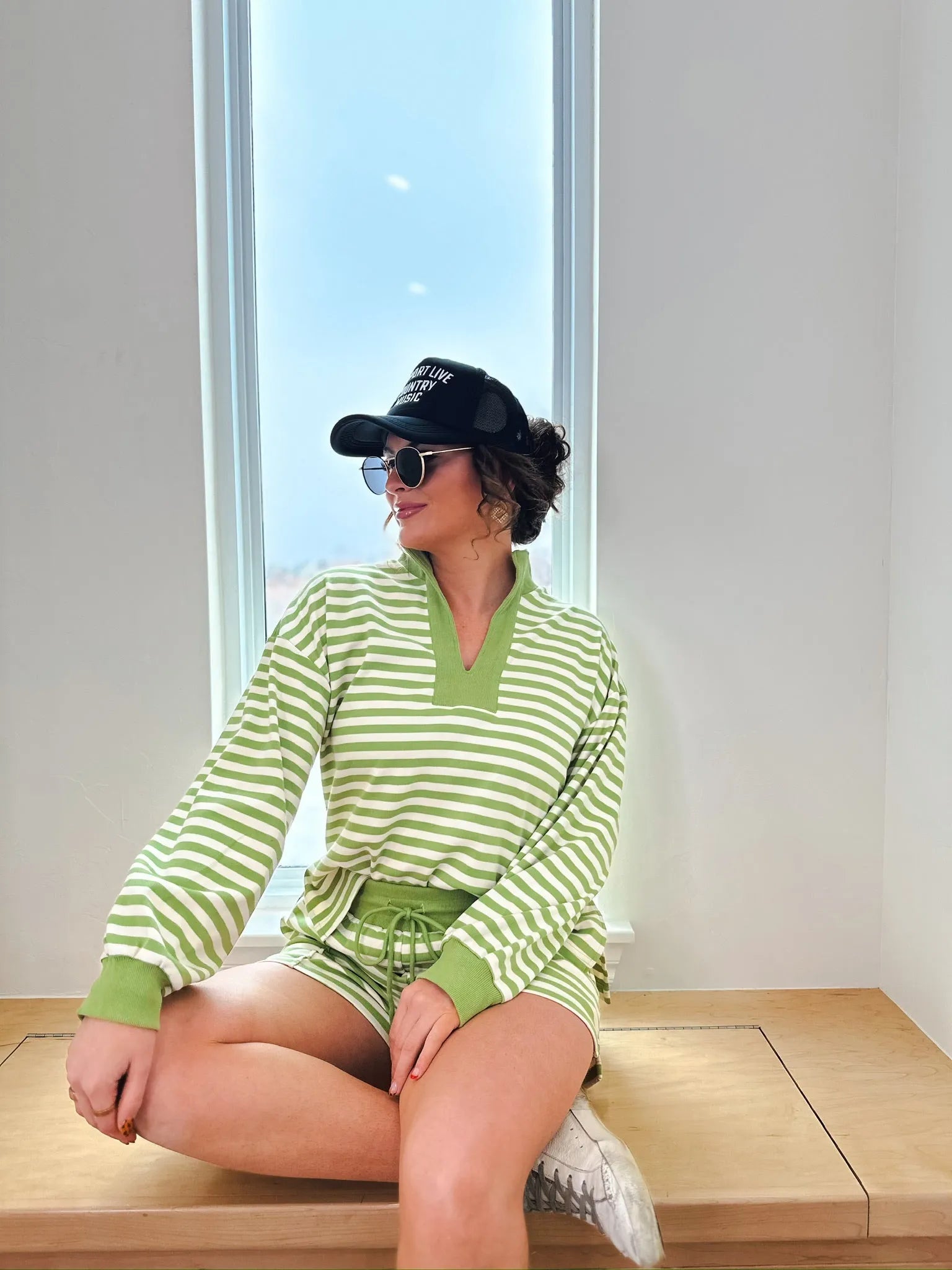 Woman wearing a green and cream striped long-sleeve pullover and matching shorts, accessorized with a black baseball cap