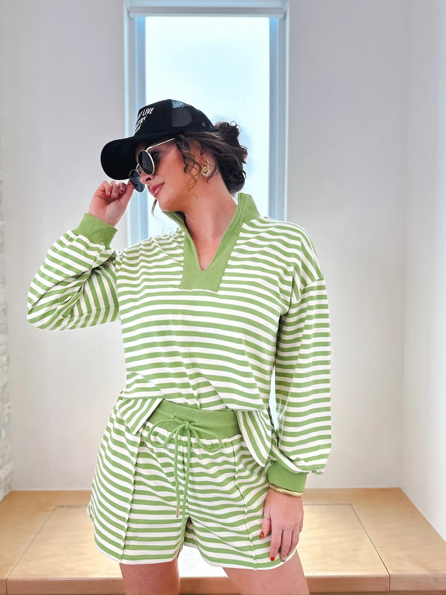 Entro green and cream striped long sleeve pullover top with drawstring shorts set. Model wears a black baseball cap and