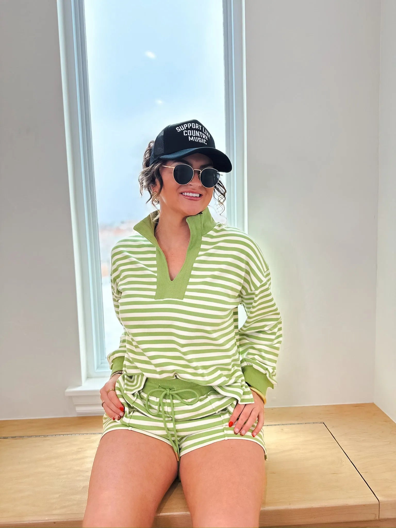 Woman wearing a green and white striped pullover long sleeve shirt and matching drawstring shorts, accessorized with