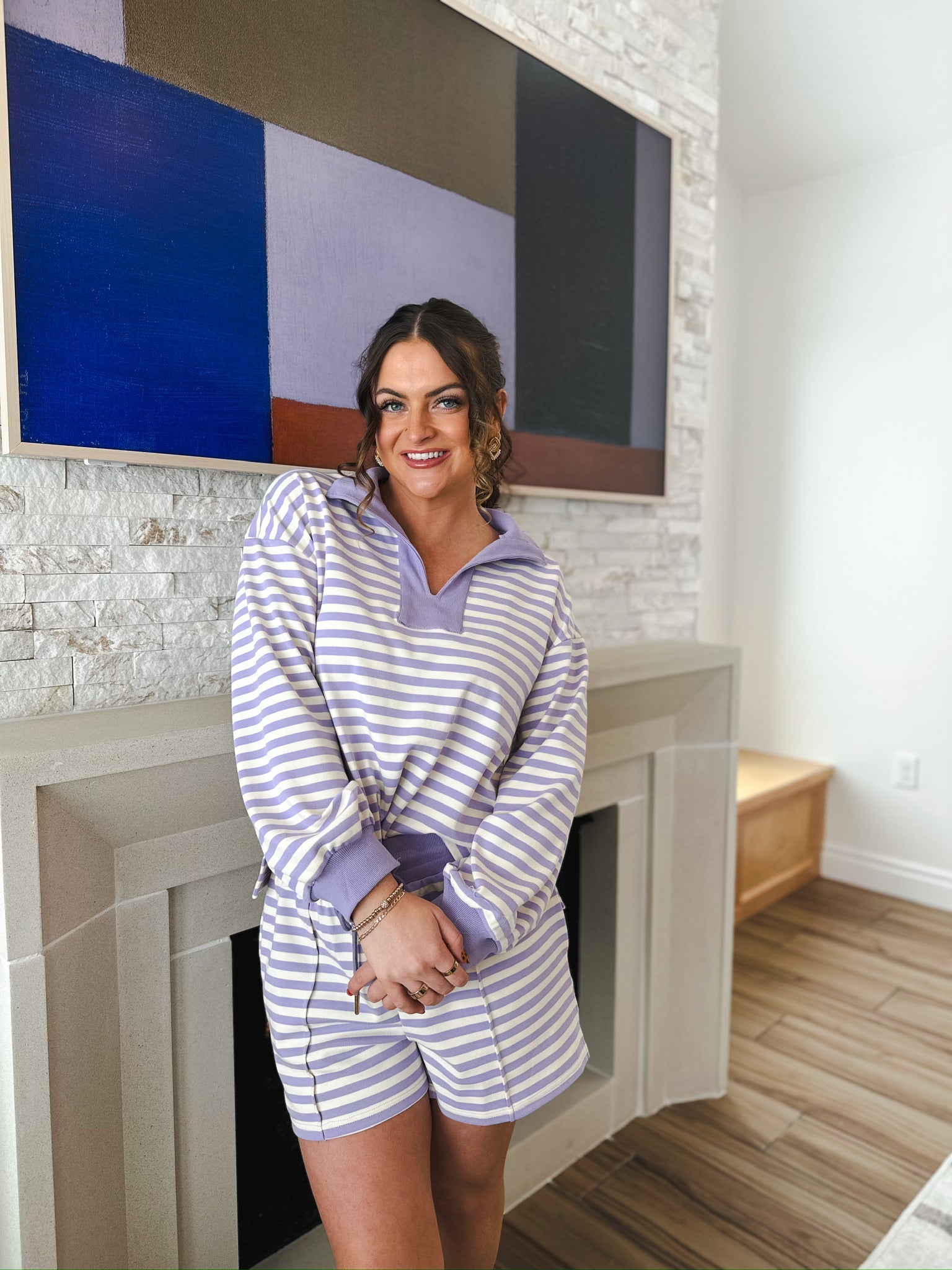 Woman wearing a lavender and cream striped pullover and shorts set. The set has a collared neckline and cuffed sleeves and