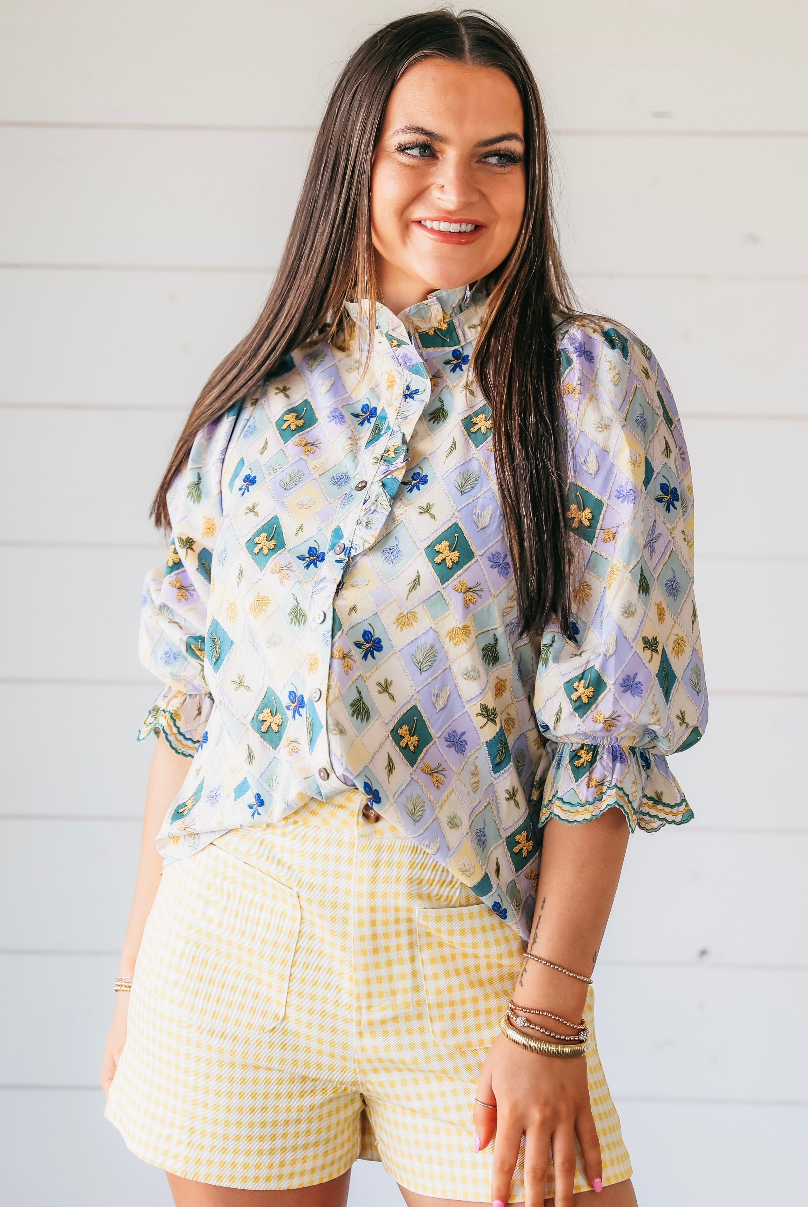 Light purple floral embroidered blouse with ruffle trim and puff sleeves, paired with yellow gingham shorts.