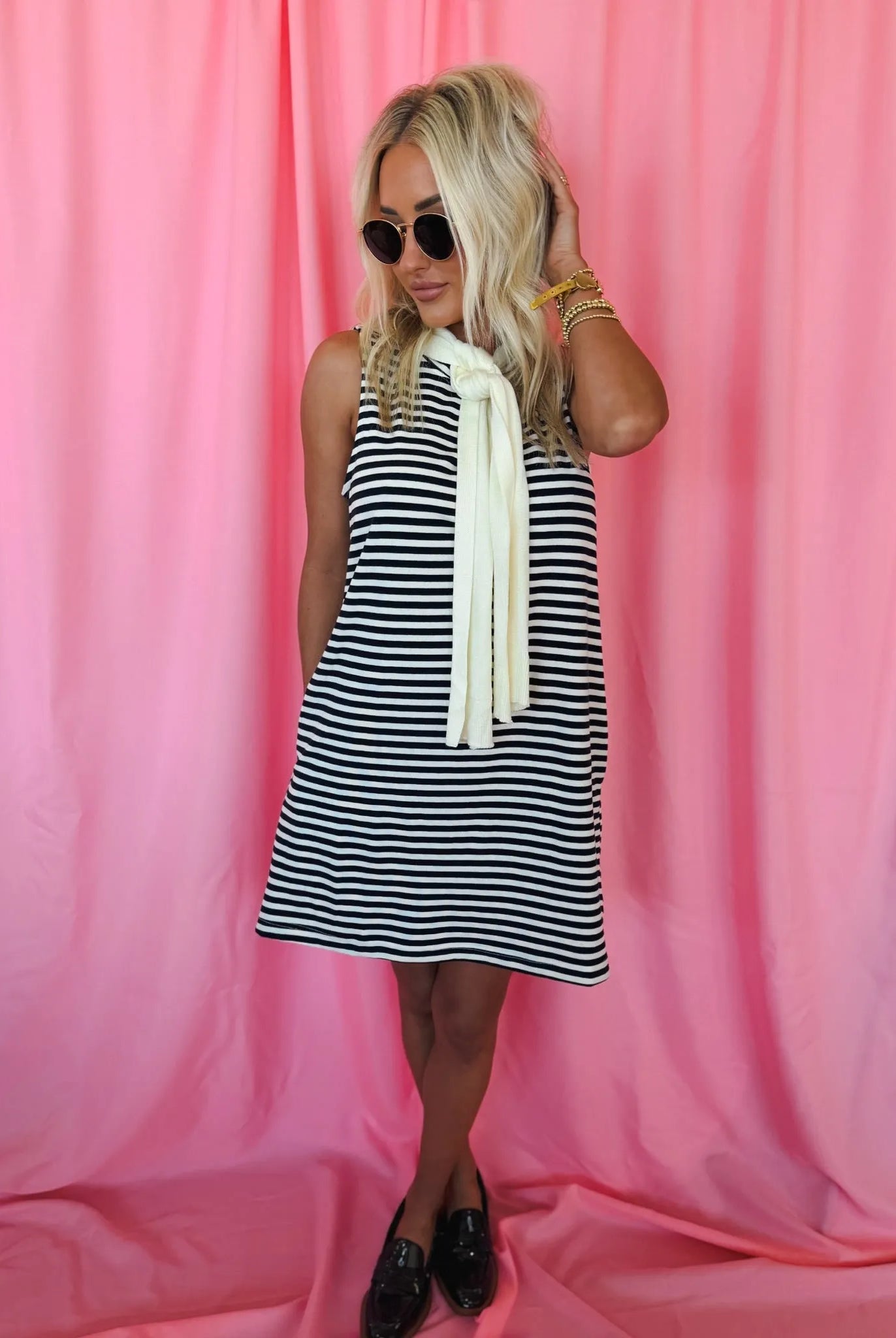 Entro Navy & Cream striped sleeveless dress with a built-in cream neck scarf. Model wearing dress, sunglasses, and black