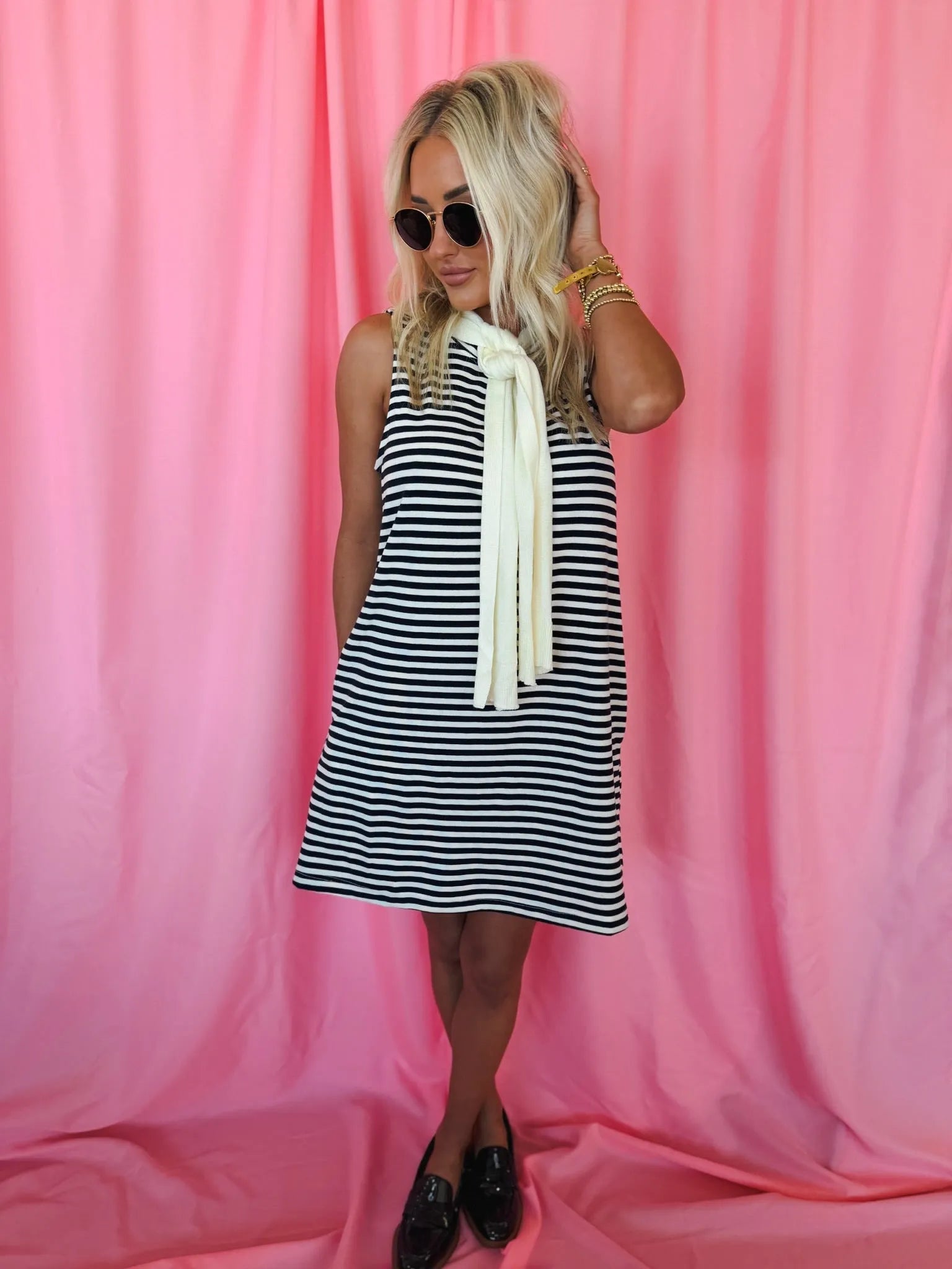 Entro Navy & Cream striped sleeveless dress with a built-in cream neck scarf. Model wearing dress, sunglasses, and black