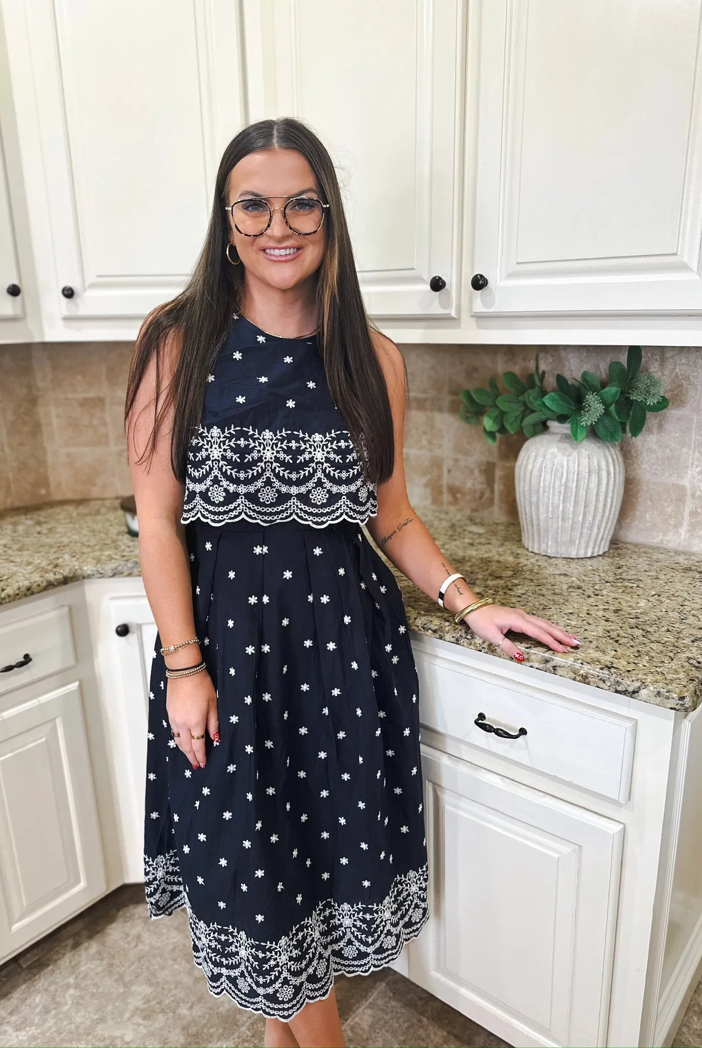 Entro navy blue sleeveless midi dress with white eyelet floral embroidery and tiered bodice. Woman wearing glasses and
