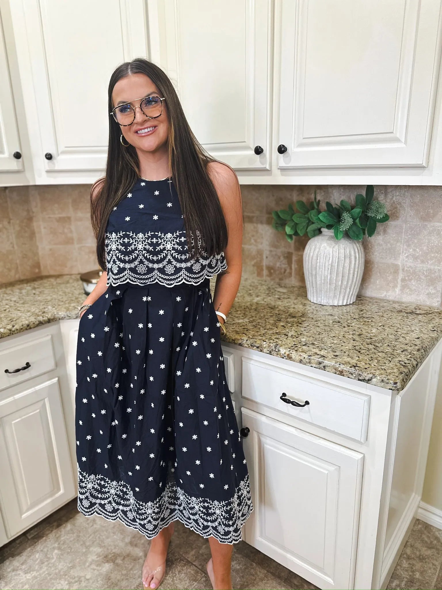 Entro navy blue sleeveless midi dress with white starburst pattern and eyelet trim. Woman wearing glasses stands in kitchen.