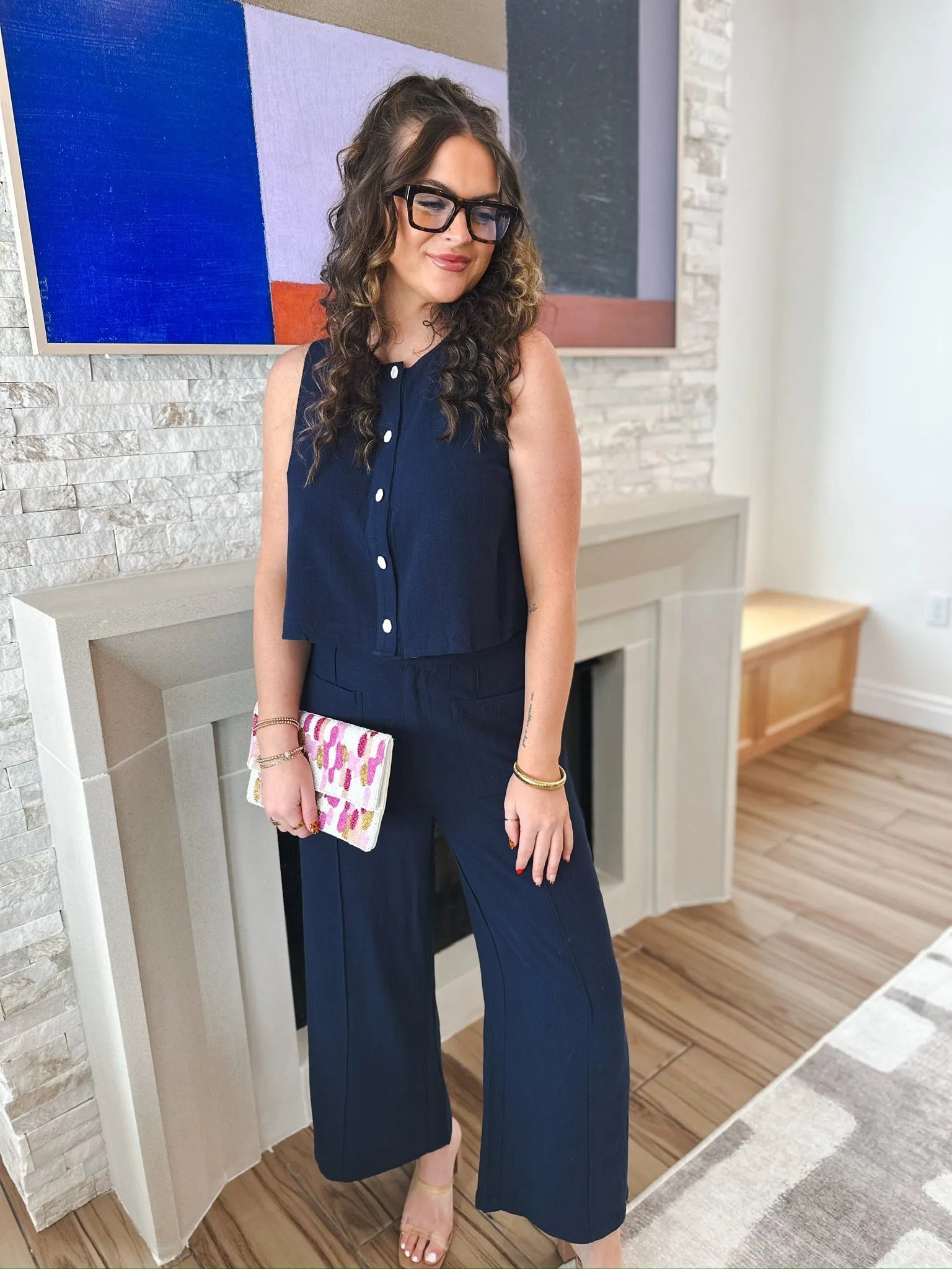 Woman wearing navy Entro trousers and matching sleeveless top, holding a colorful clutch.