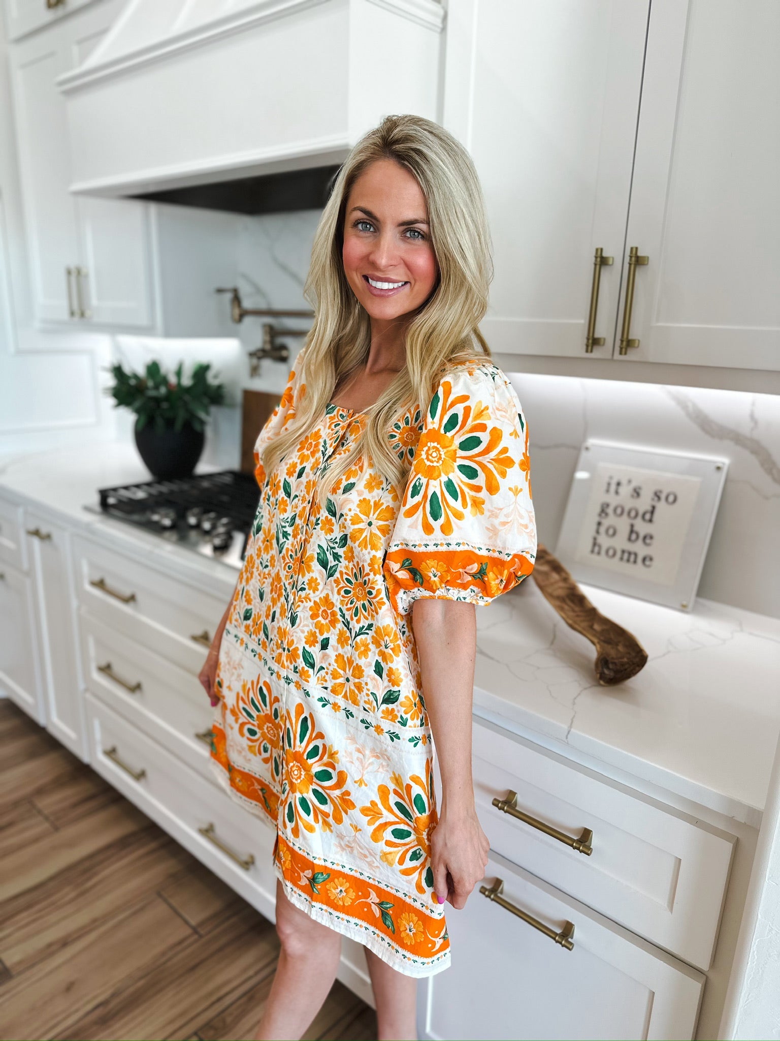 Woman in Entro orange floral puff sleeve mini dress with a white background featuring orange and green floral patterns.